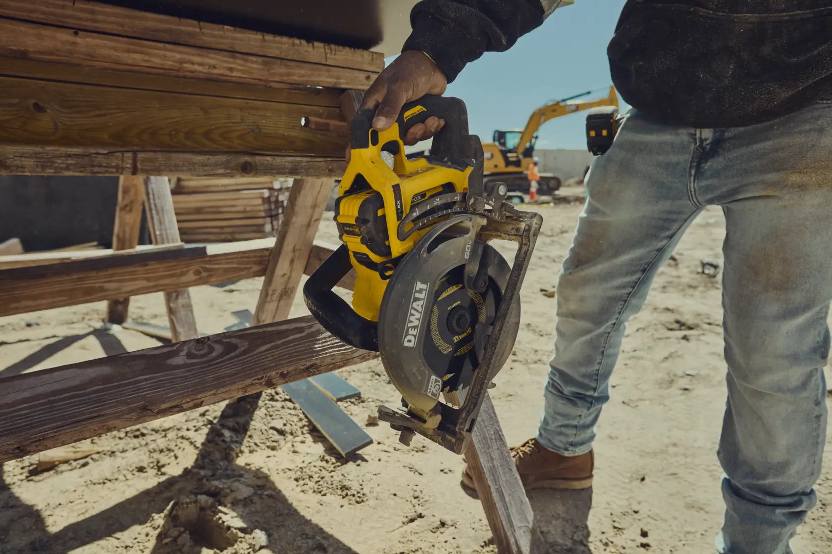 A construction worker holding a DEWALT cordless circular saw next to a wooden structure at an outdoor job site.