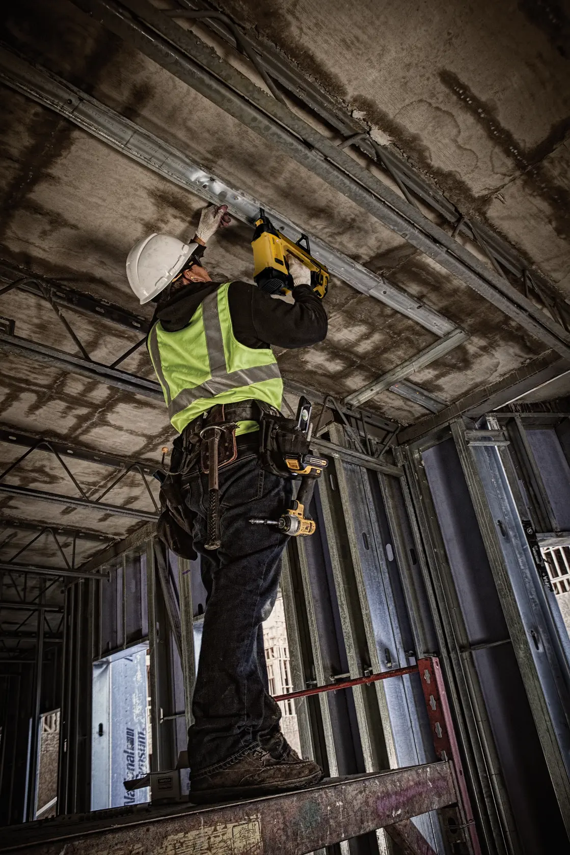 Worker uses DEWALT DGN845D1-QW and DGN845D1 on ceiling at construction site. Photography product category.