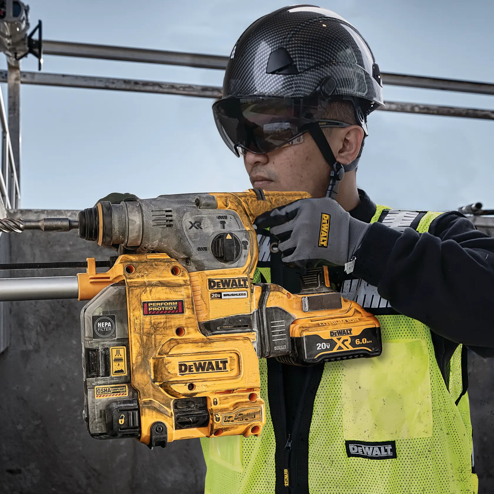 A person wearing safety gear, including a helmet and high-visibility vest, is operating a DEWALT cordless rotary hammer drill at a construction site. The DEWALT branding and various safety and performance labels are visible on the tool.
