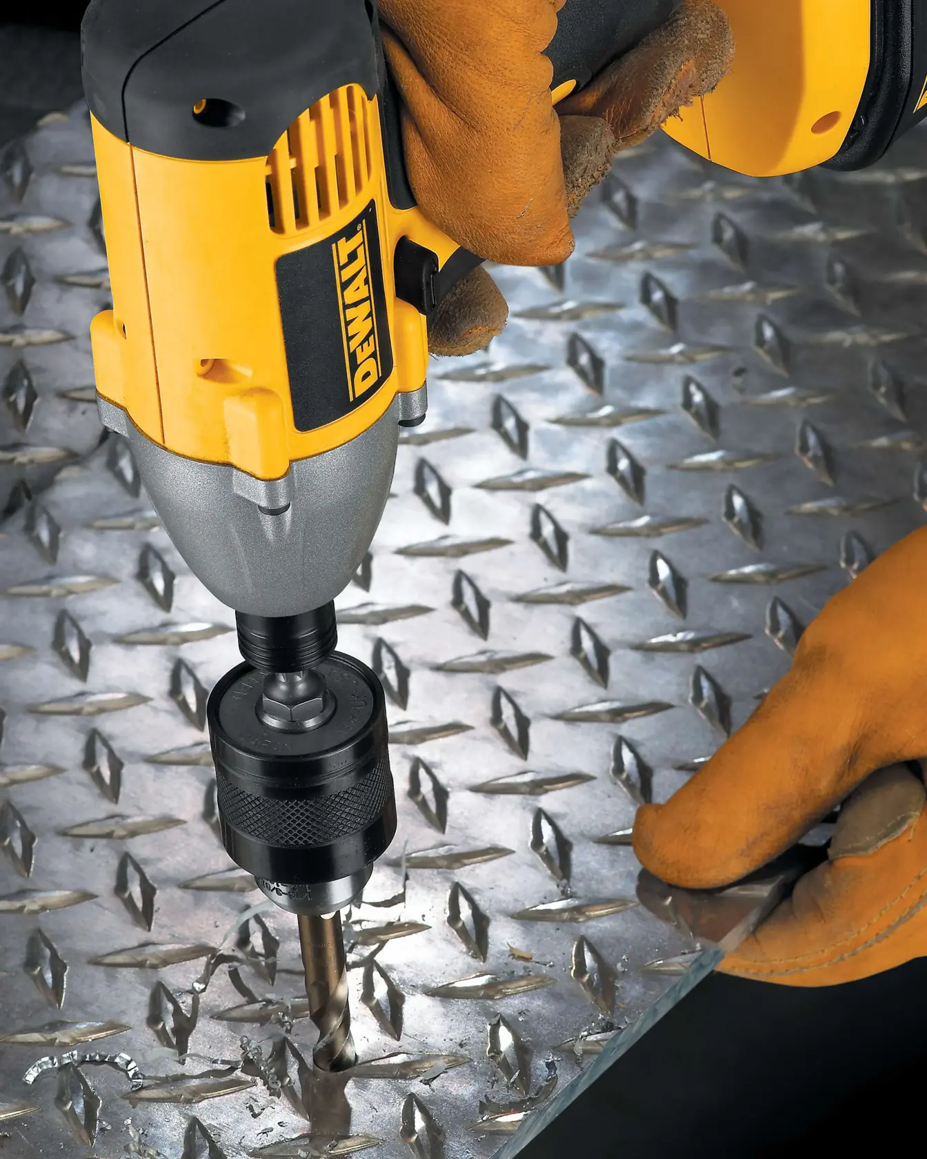 A close-up image of a DEWALT power drill being used with a drill bit to make a hole in a metal diamond plate sheet. The person operating the drill is wearing brown work gloves.