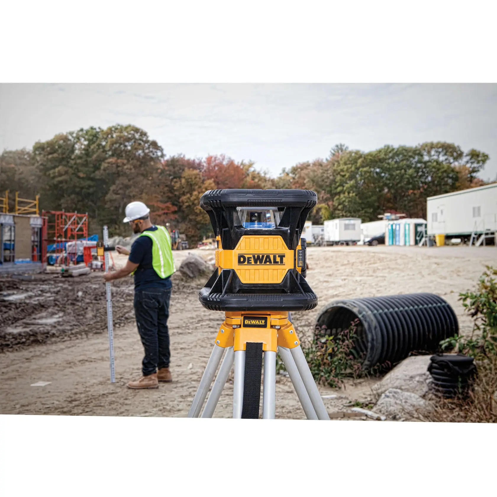 Red rotary tough laser mounted on a tripod being used at a construction site.