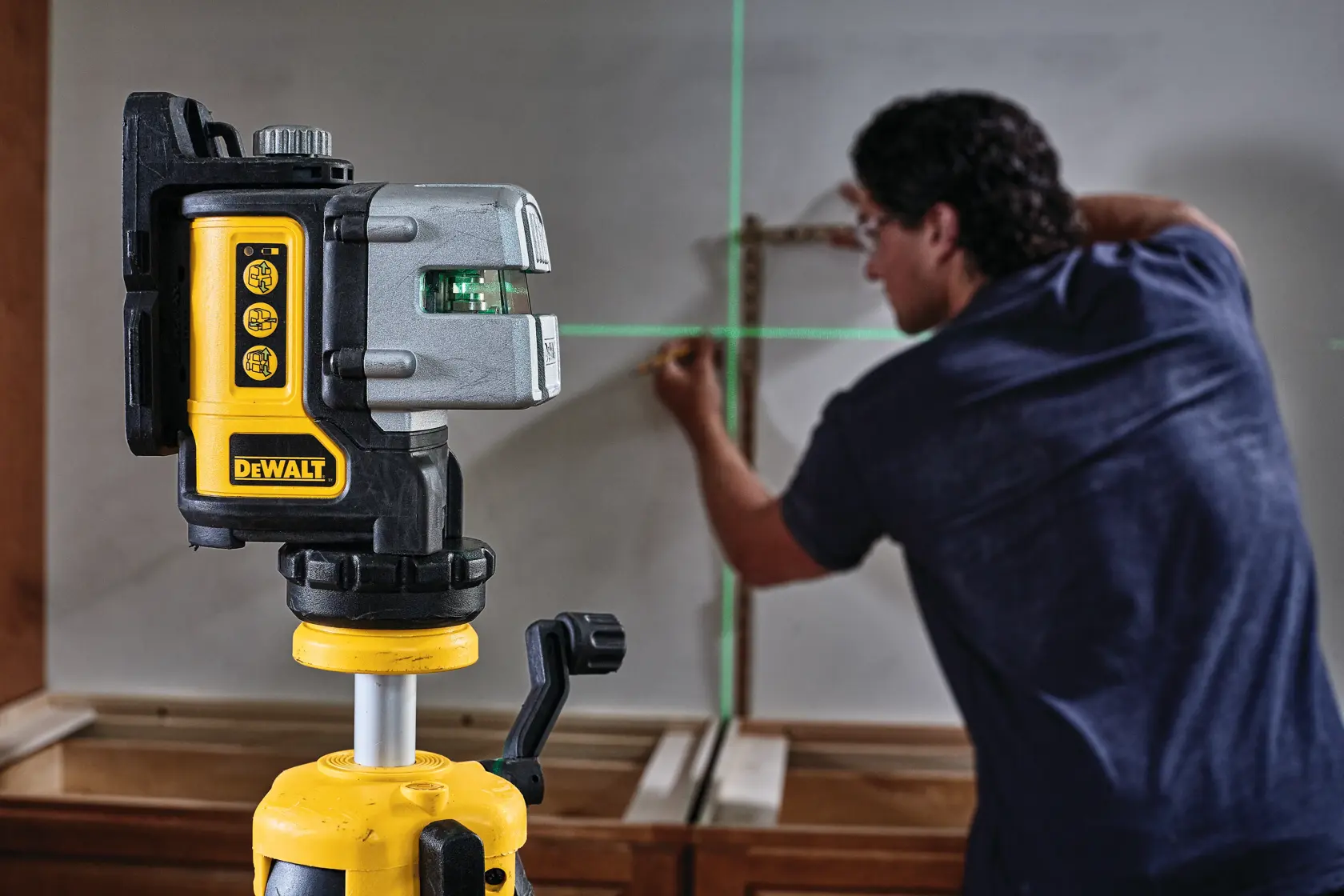 3 line green laser level mounted on a tripod and being used by a construction worker.