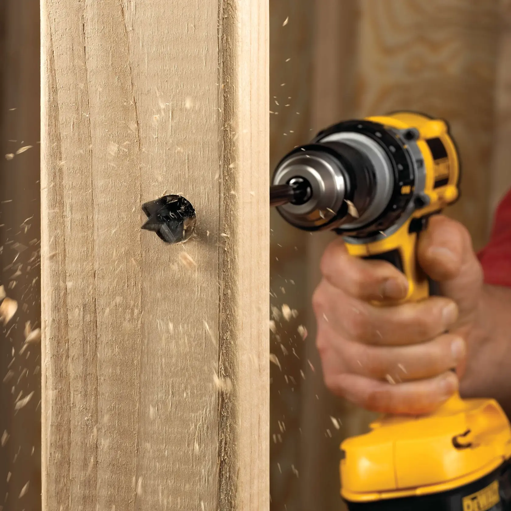 28.5 millimeters spade bit attached to a drill and drilling a hole through a wooden plank.