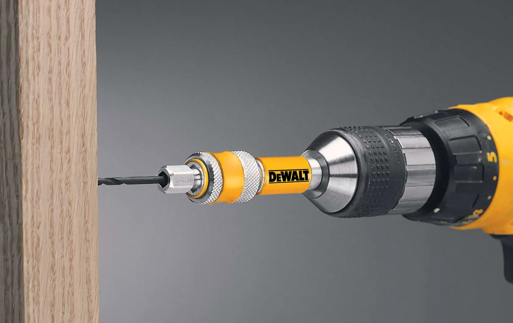 A DEWALT drill with a bit holder attachment is shown drilling into a wooden surface.