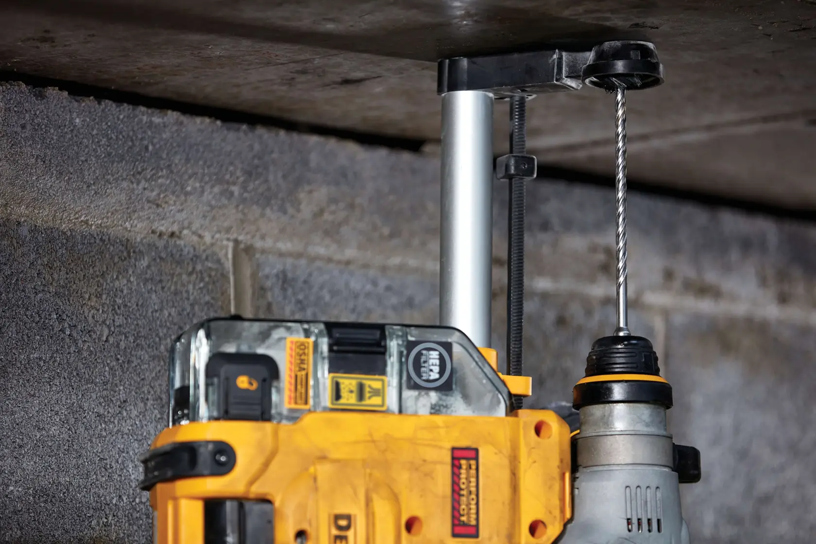 Close-up of a DEWALT power drill with an attached drilling guide, being used to drill into a concrete ceiling.