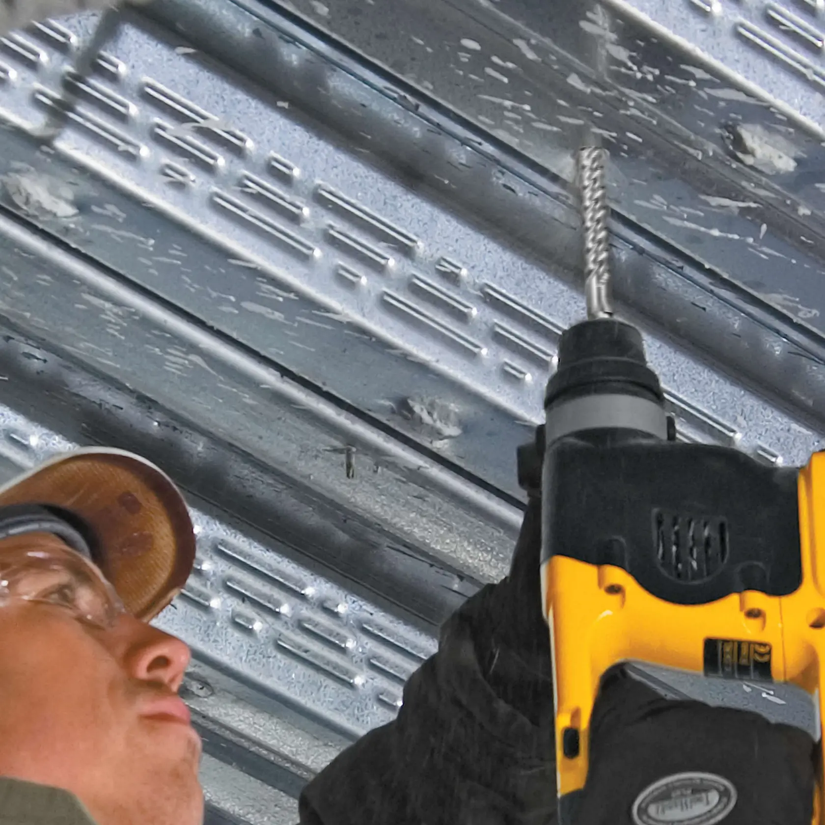 Close up of three eighths inch by 4 inch by 6 and half inch S D S Plus Full Head Carbide Drill Bit being used by worker to drill through metal ceiling.