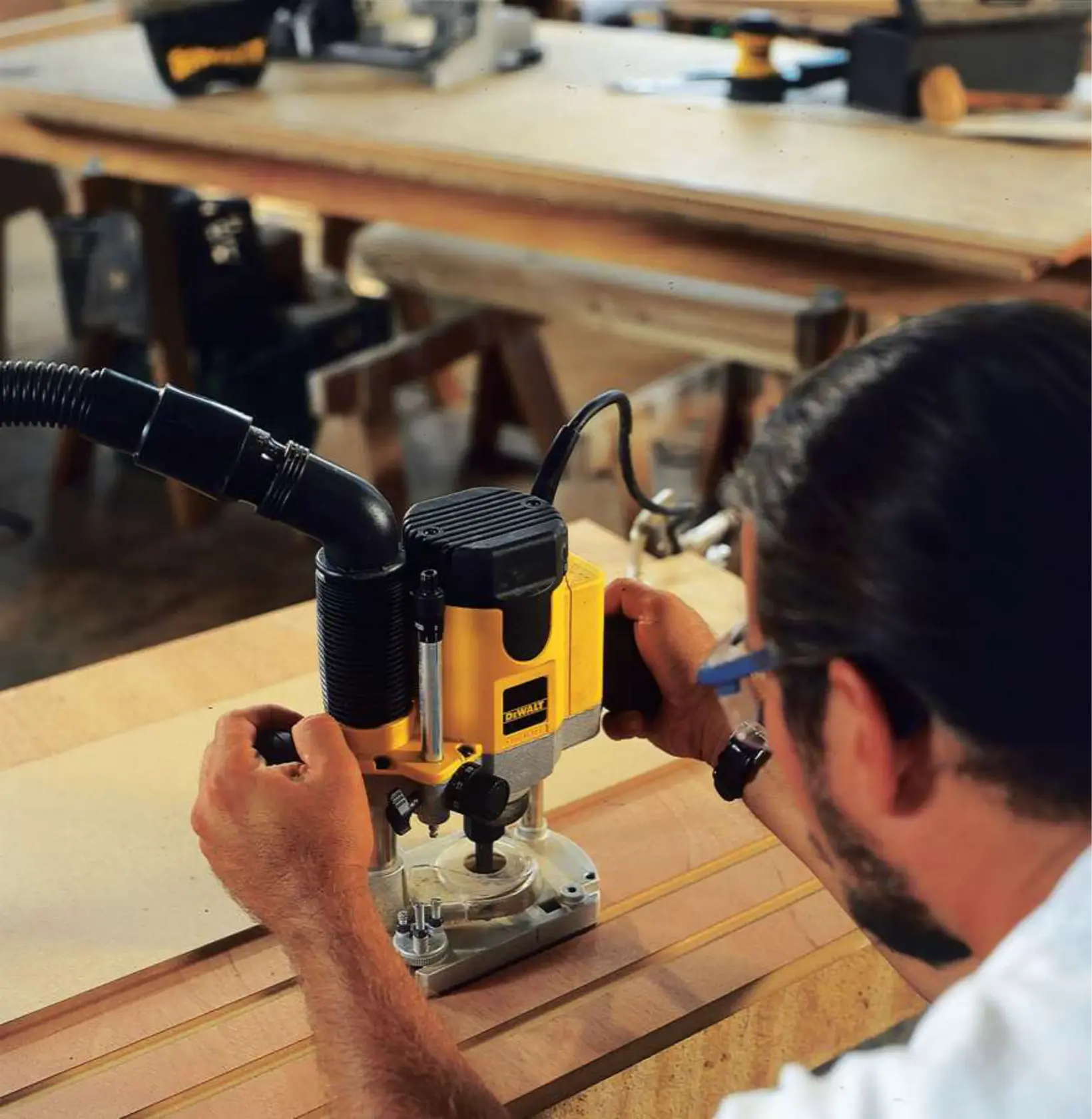 Person uses a DEWALT DW621 router for woodworking on a table, in a workshop setting.
