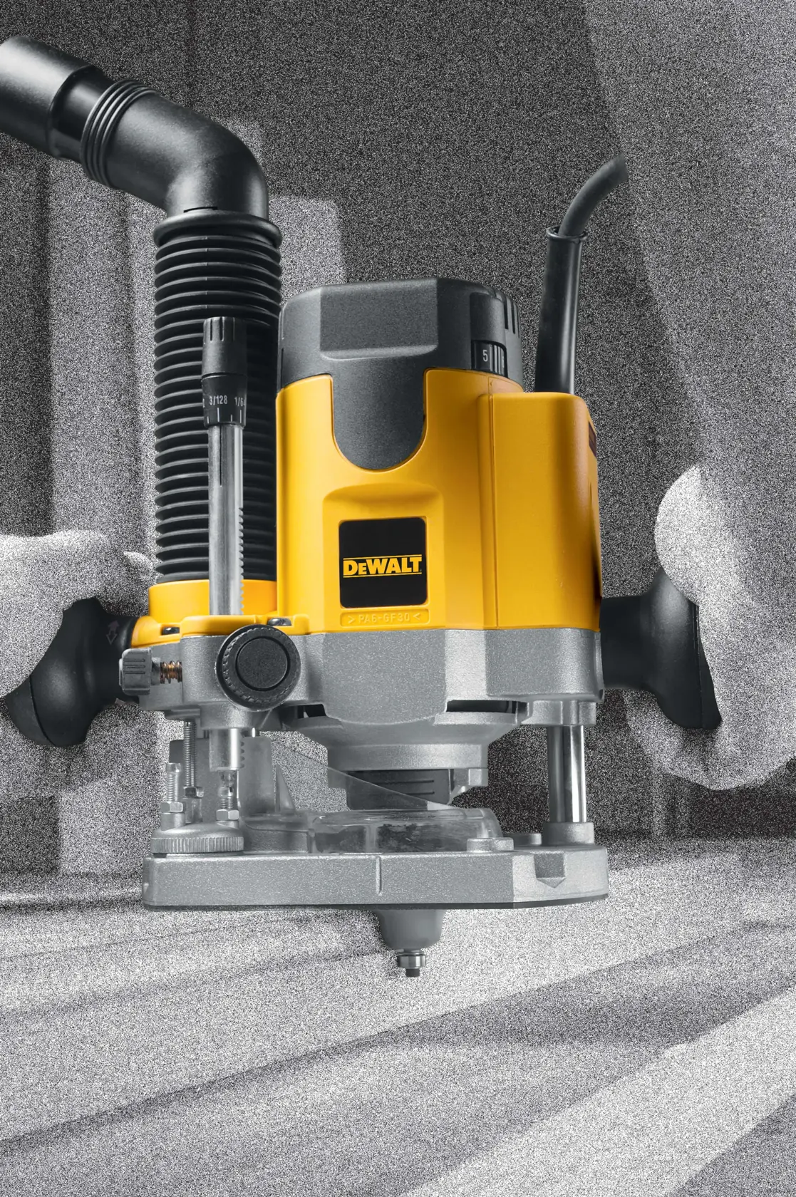 A DEWALT DW621 plunge router is being operated, with a yellow and black body, attached to a hose for dust extraction. The router is being used to work on a wooden surface.