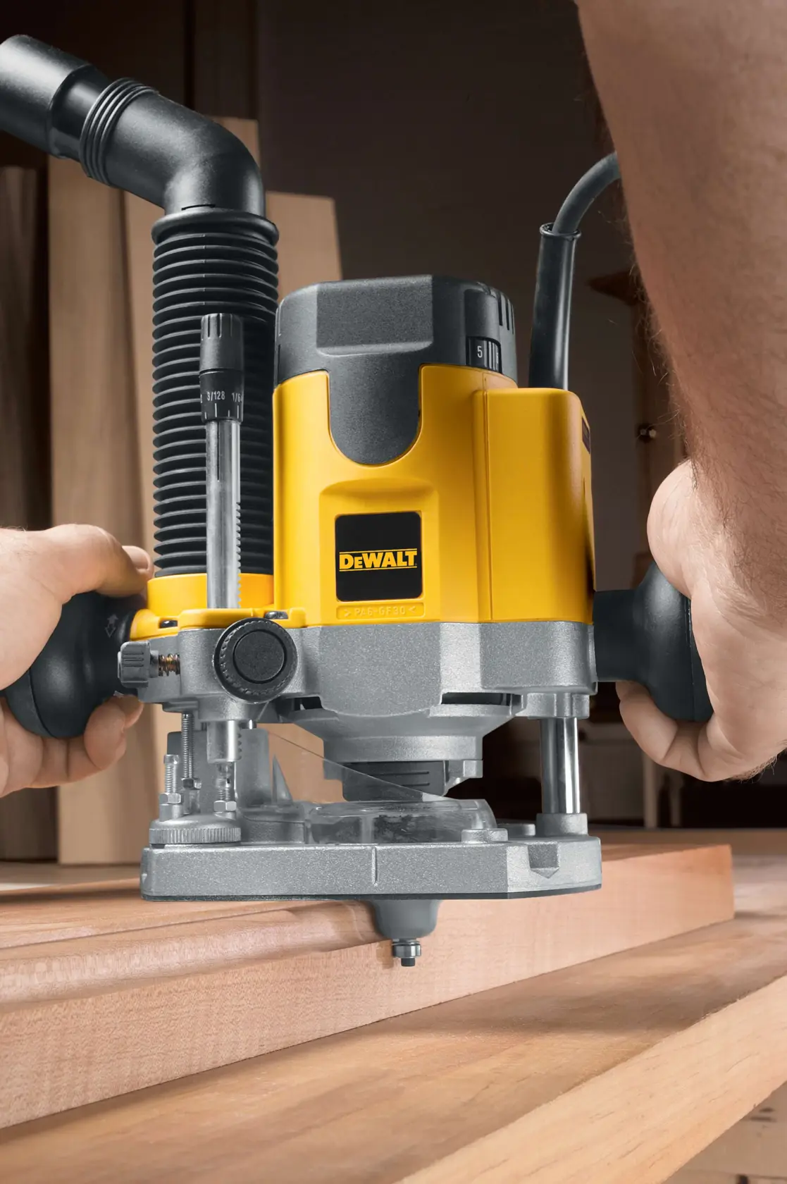 Close-up of a DEWALT DW621 router being used on a wooden surface, with hands holding the tool and a dust extraction hose attached.