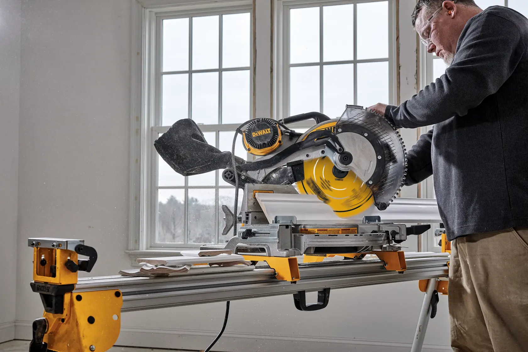 A person cutting a wooden plank using a DEWALT miter saw inside a workshop.