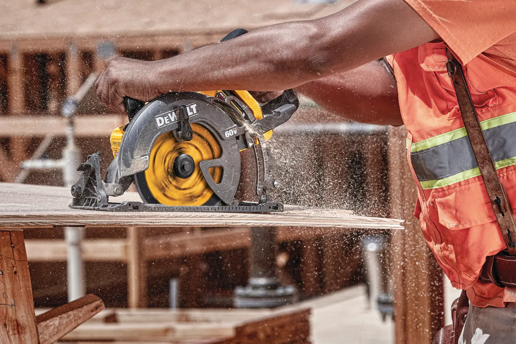 A person wearing an orange safety vest is using a DEWALT circular saw to cut a wooden board. Sawdust is flying as the saw operates on a construction site.