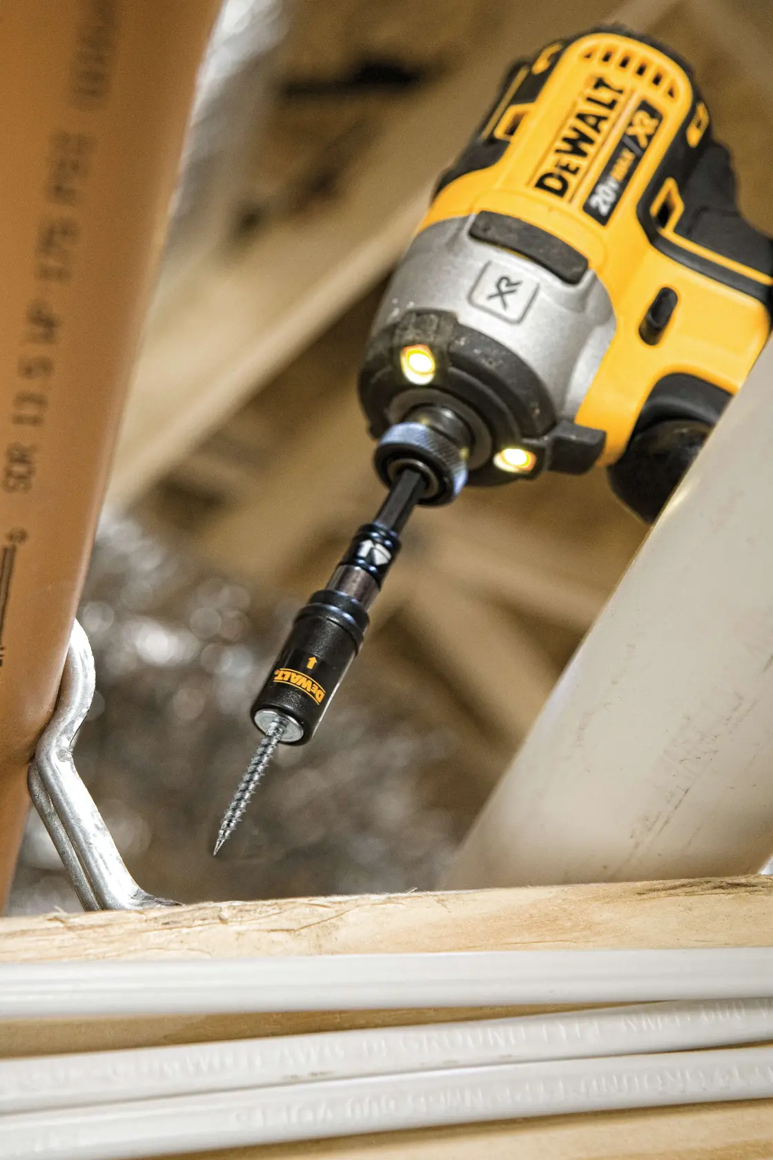 A close-up of a DEWALT cordless drill with a screwdriving bit, being used to drive a screw into a wooden surface in a construction or renovation setting.