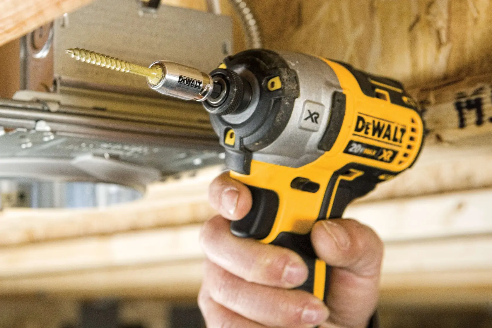 A close-up of a hand using a DEWALT 20V MAX XR cordless power drill with a screwdriver bit to drive a screw into a wooden beam.