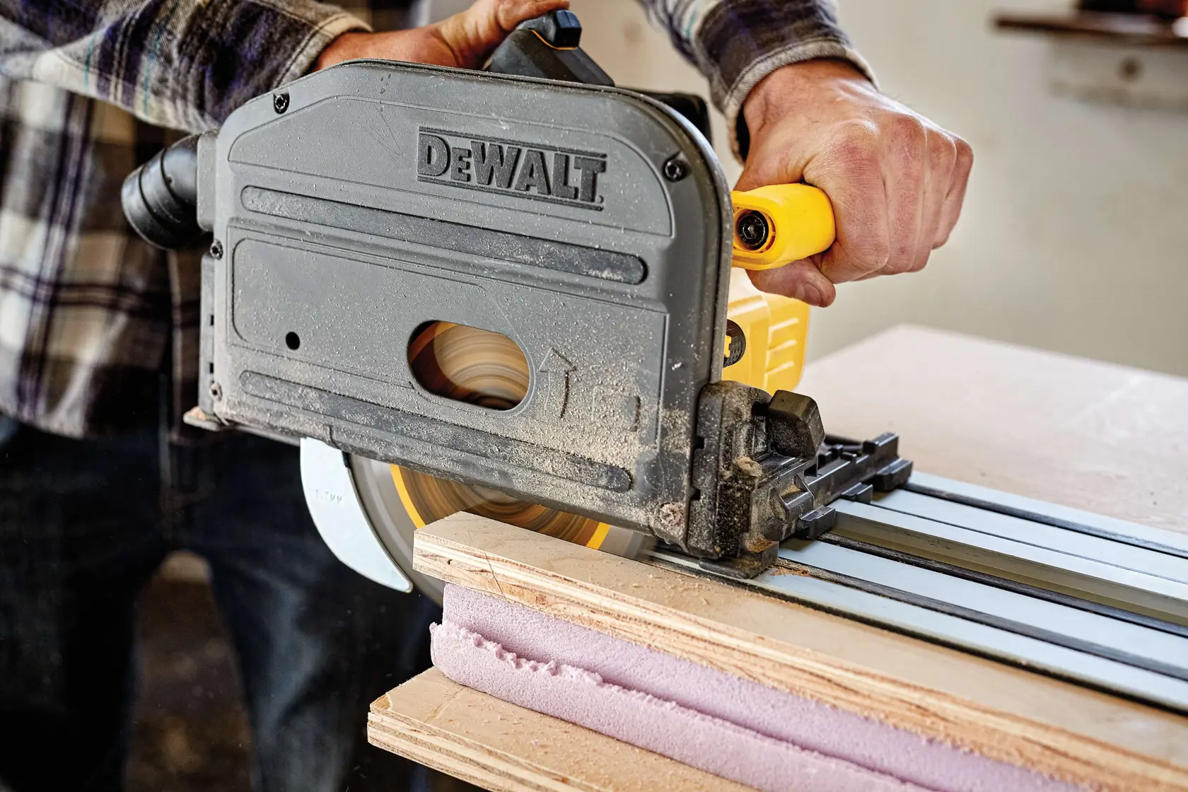 A close-up view of a person using a DEWALT track saw to cut through a piece of wood on a guide rail.
