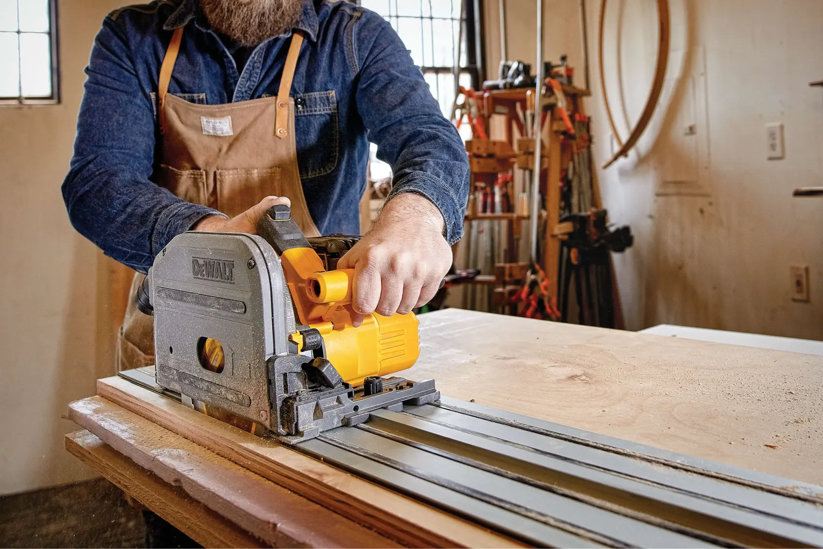 A person using a DEWALT track saw to cut a sheet of wood in a workshop.
