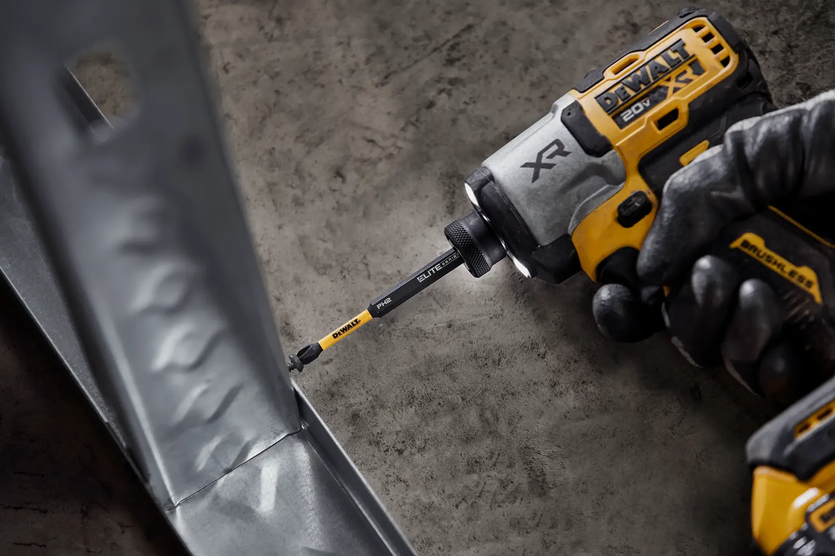 A close-up of a person wearing gloves using a DEWALT 20V XR cordless impact driver with a DEWALT Elite Series bit to fasten a screw into a metal frame.