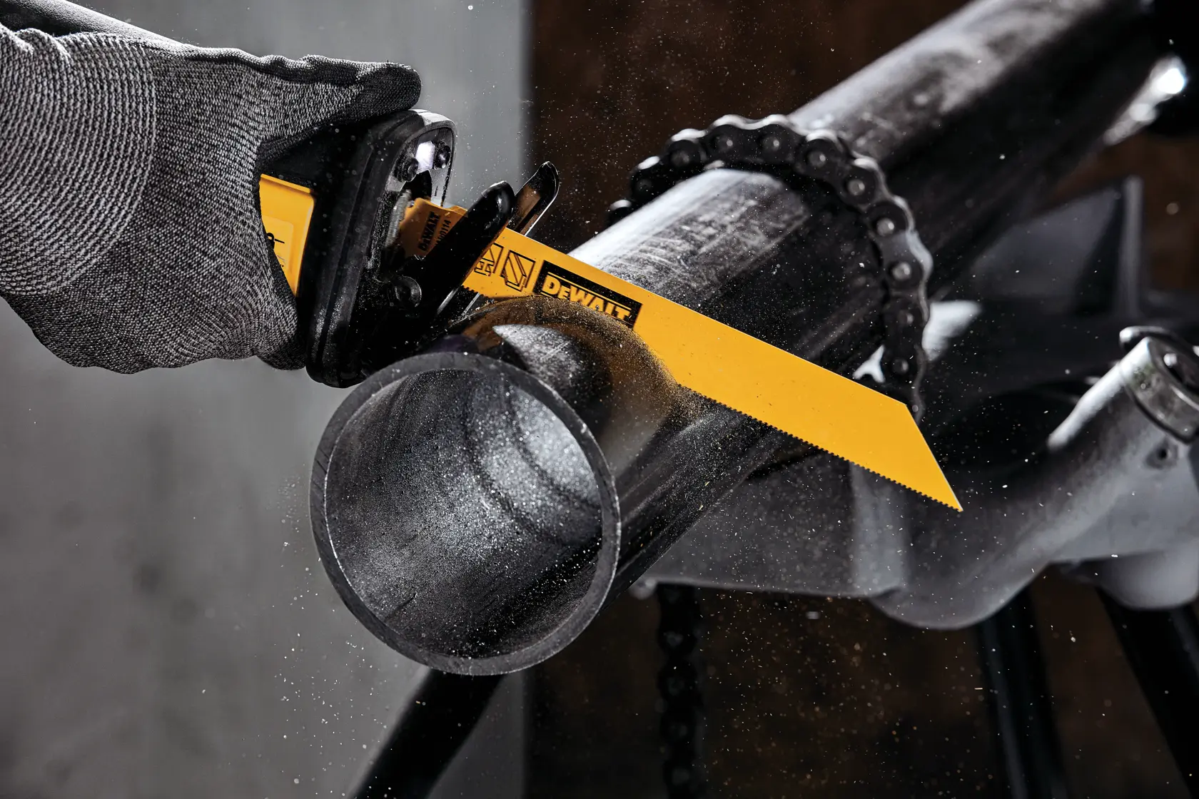 A gloved hand using a DEWALT reciprocating saw with a yellow blade to cut through a metal pipe, with metal particles flying.