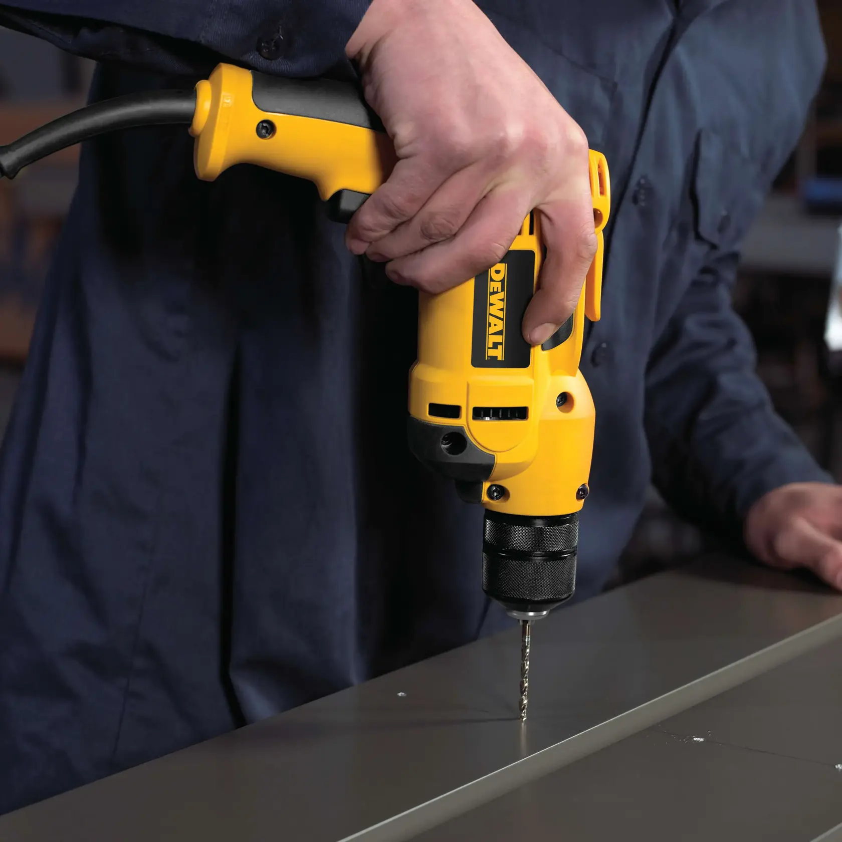 A person using a yellow electric drill to make holes in a metal surface.