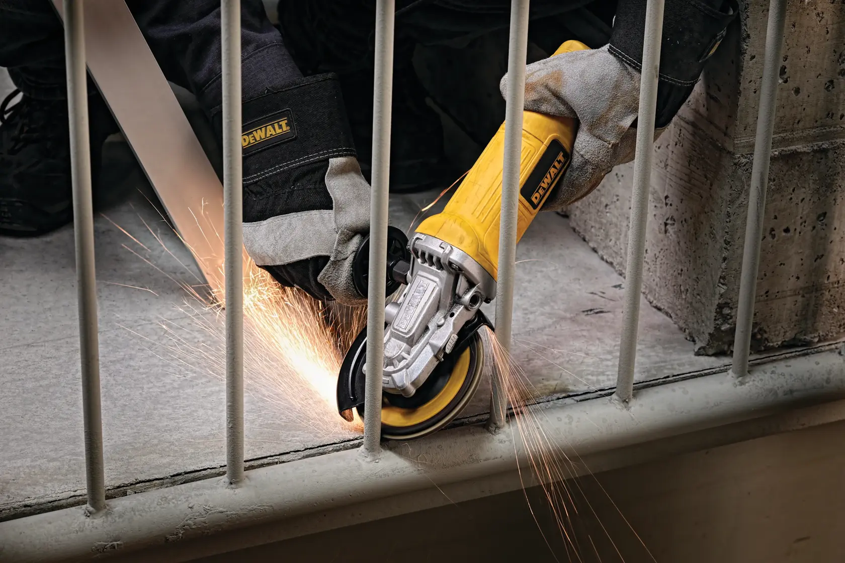A person wearing protective gloves uses a DEWALT angle grinder to cut through a metal railing, creating sparks.