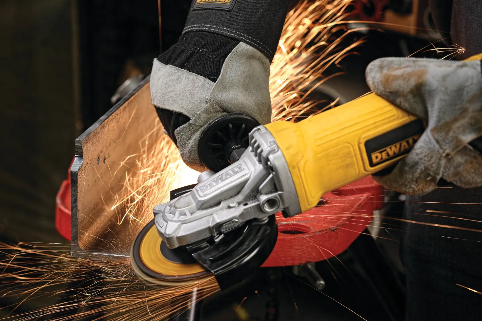 A person wearing protective gloves using a DEWALT yellow angle grinder to cut or grind a metal piece, with sparks flying from the tool.