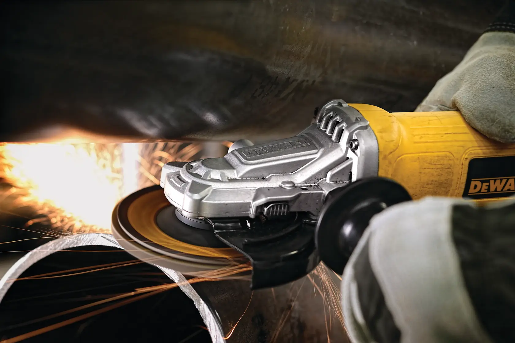 A close-up of a DEWALT angle grinder in use, cutting through metal with sparks flying. The person operating the grinder is wearing gloves.