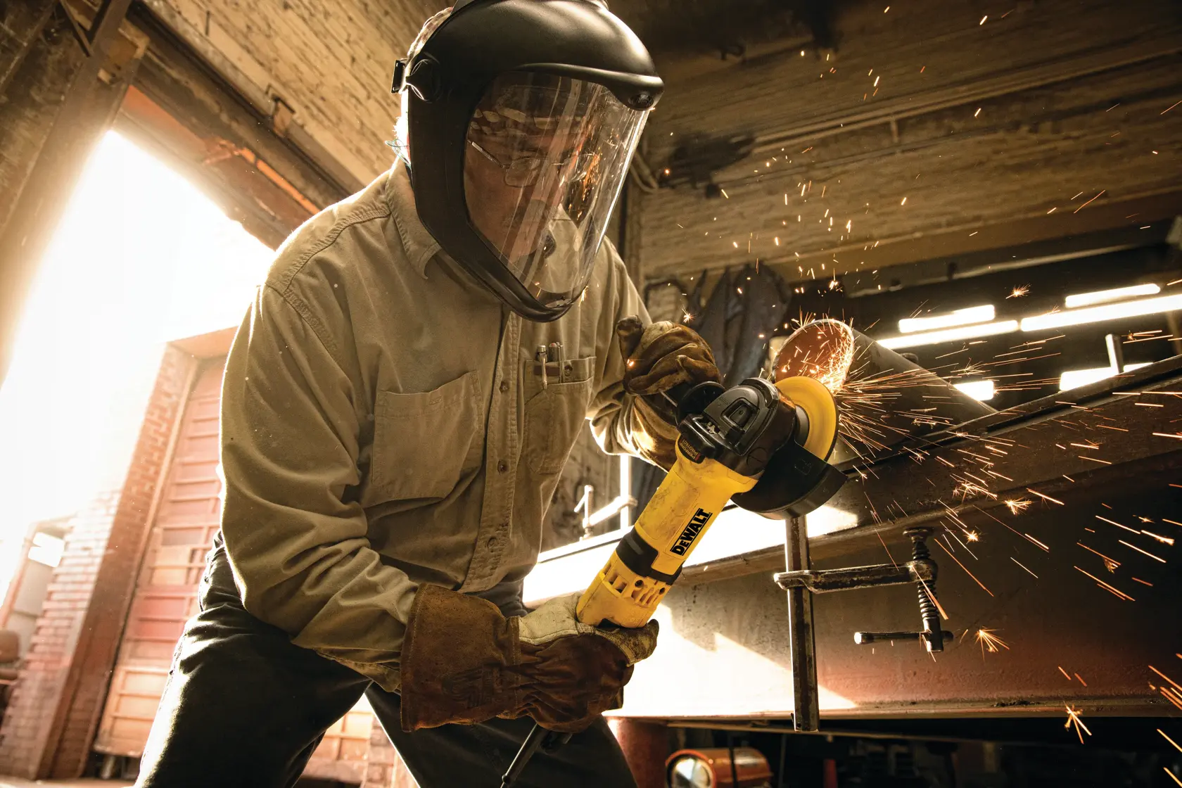 A person wearing protective gear is using a yellow DEWALT angle grinder to cut metal, with sparks flying in a workshop setting.