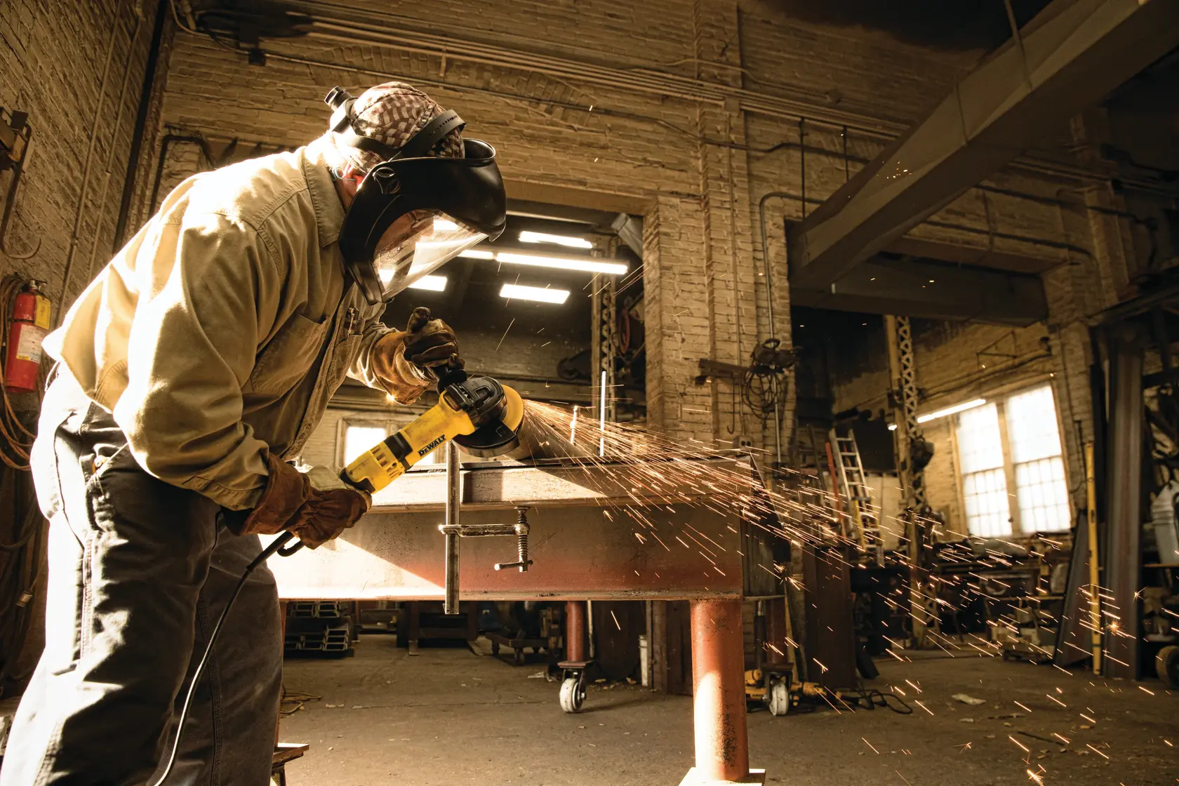 A person wearing protective gear uses a yellow DEWALT angle grinder to cut metal in a workshop, producing visible sparks.
