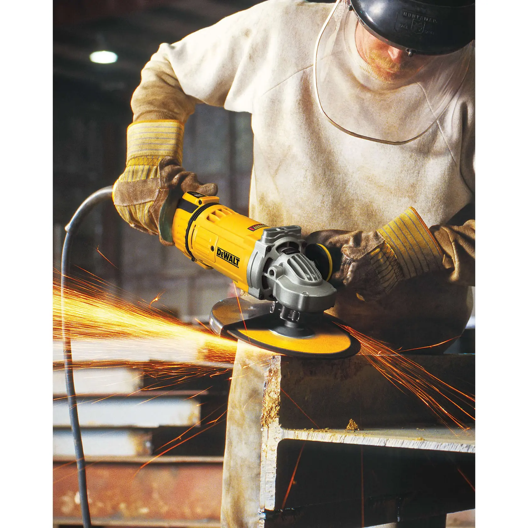 A worker wearing protective clothing, gloves, and a face shield is using a yellow DEWALT angle grinder on a piece of metal, generating sparks in an industrial setting.