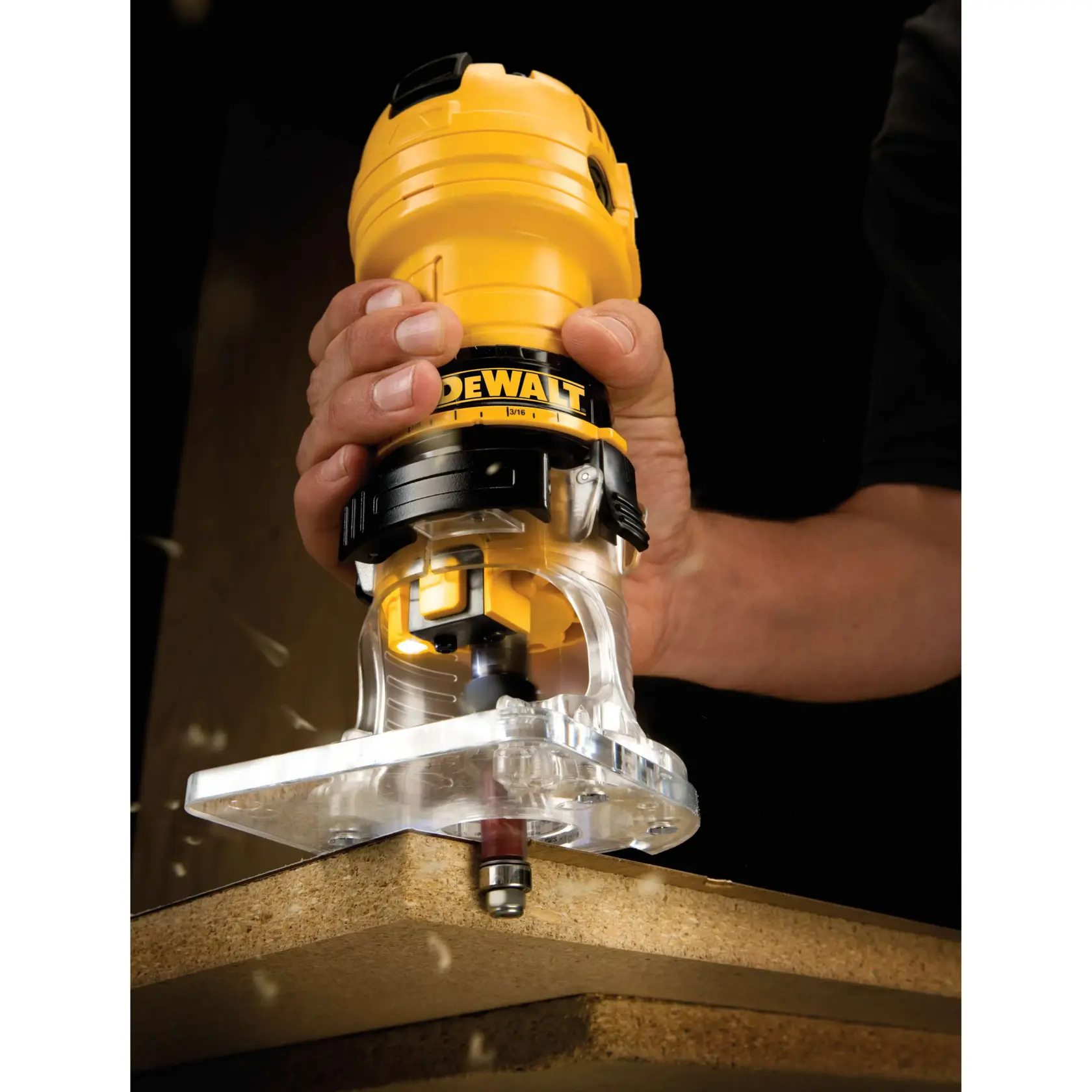A close-up image of a DEWALT DWE6000 compact router being used to trim the edge of a wooden board, held by a person's hand.