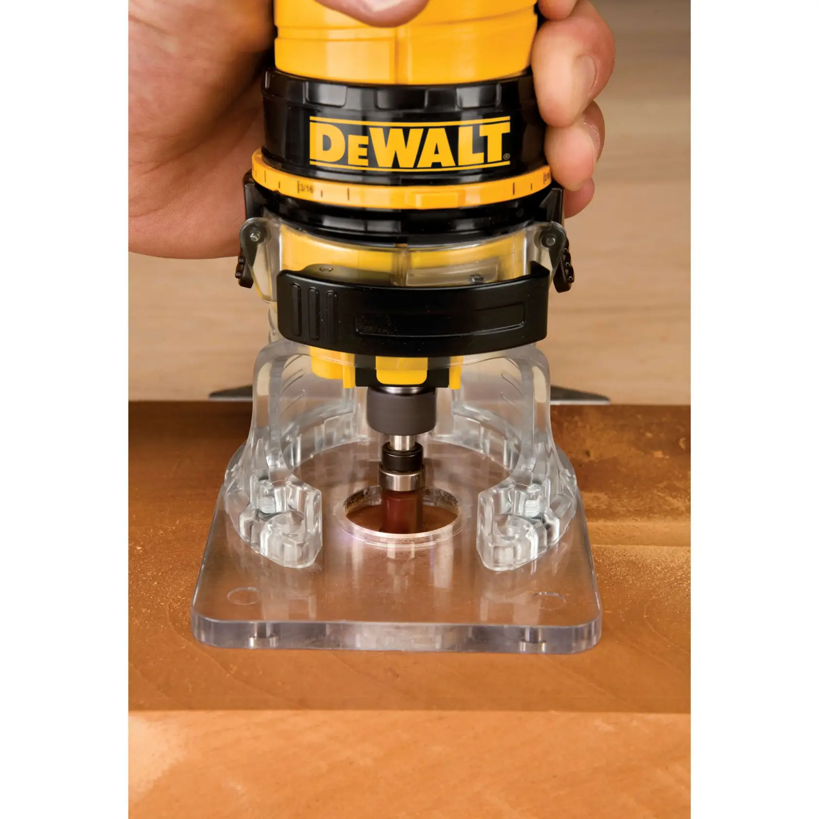 A close-up image of a person using a DEWALT handheld router with a clear base plate to trim or shape the edge of a piece of wood.