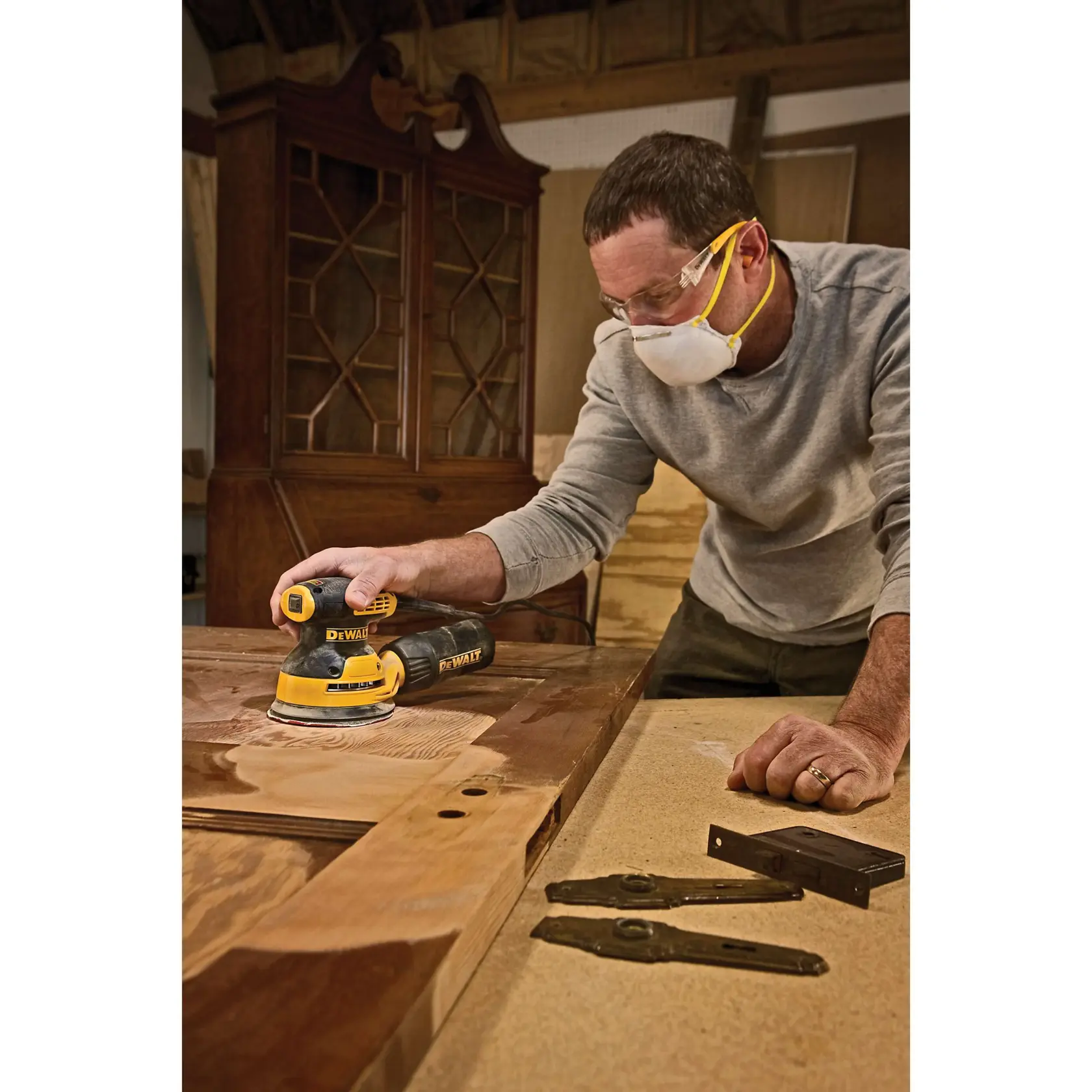 A close-up of hands attaching a sanding disc to a yellow and black DEWALT electric sander on a wooden surface.