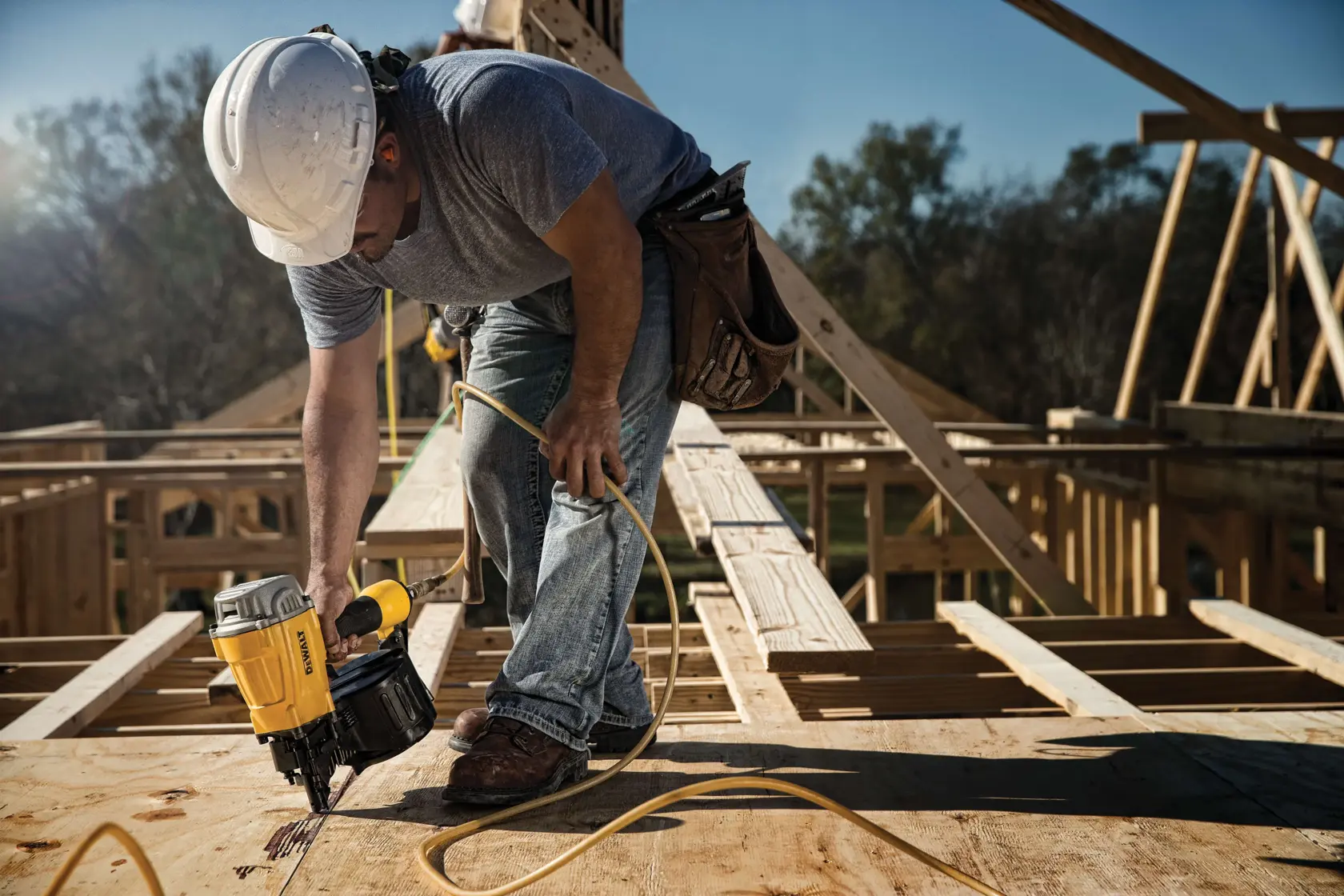 Coil framing nailer being used by a person to fasten into wooden surface.