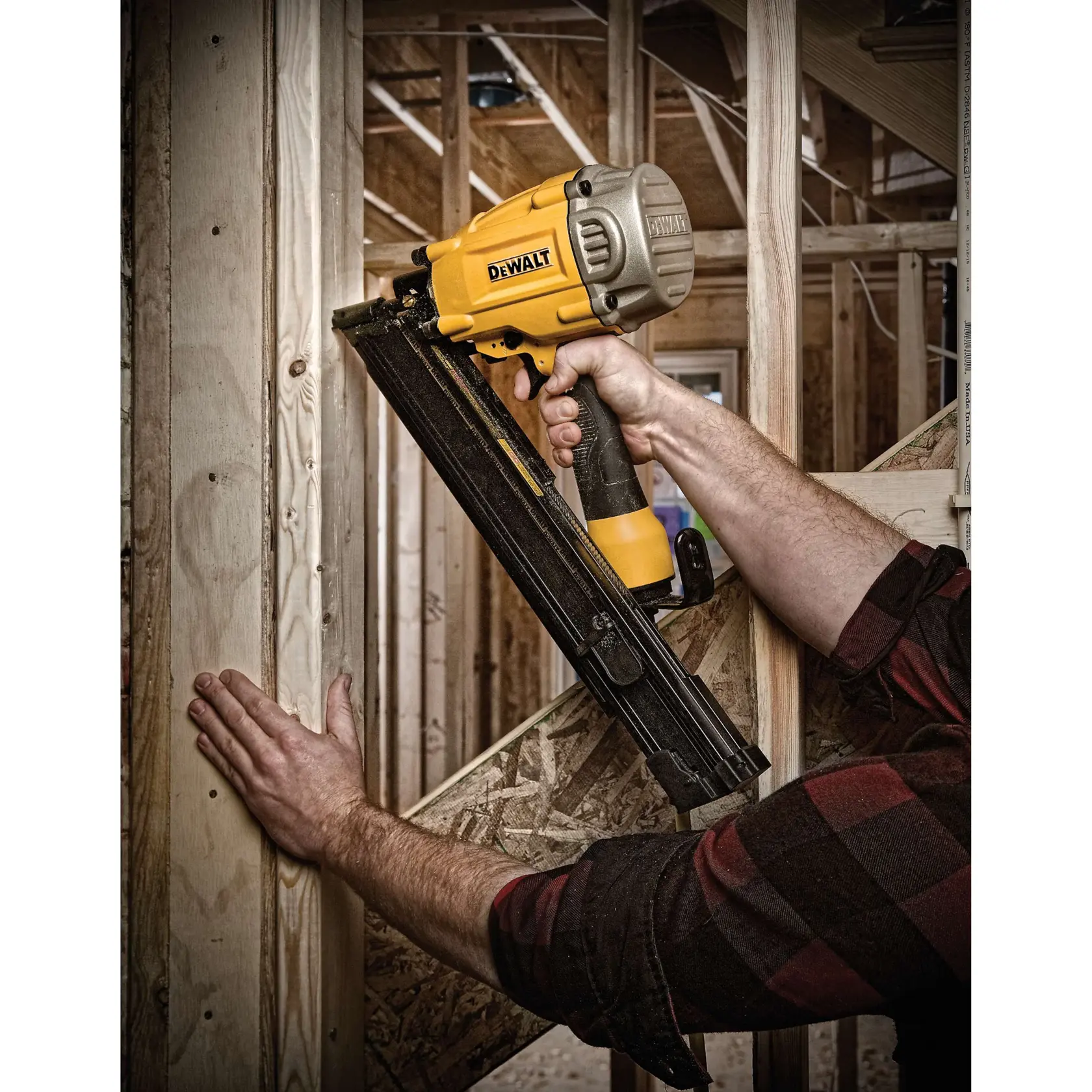 A person using a DEWALT pneumatic framing nailer to secure wooden beams in a construction setting. The tool is yellow and black, and the scene shows wood framing in progress.