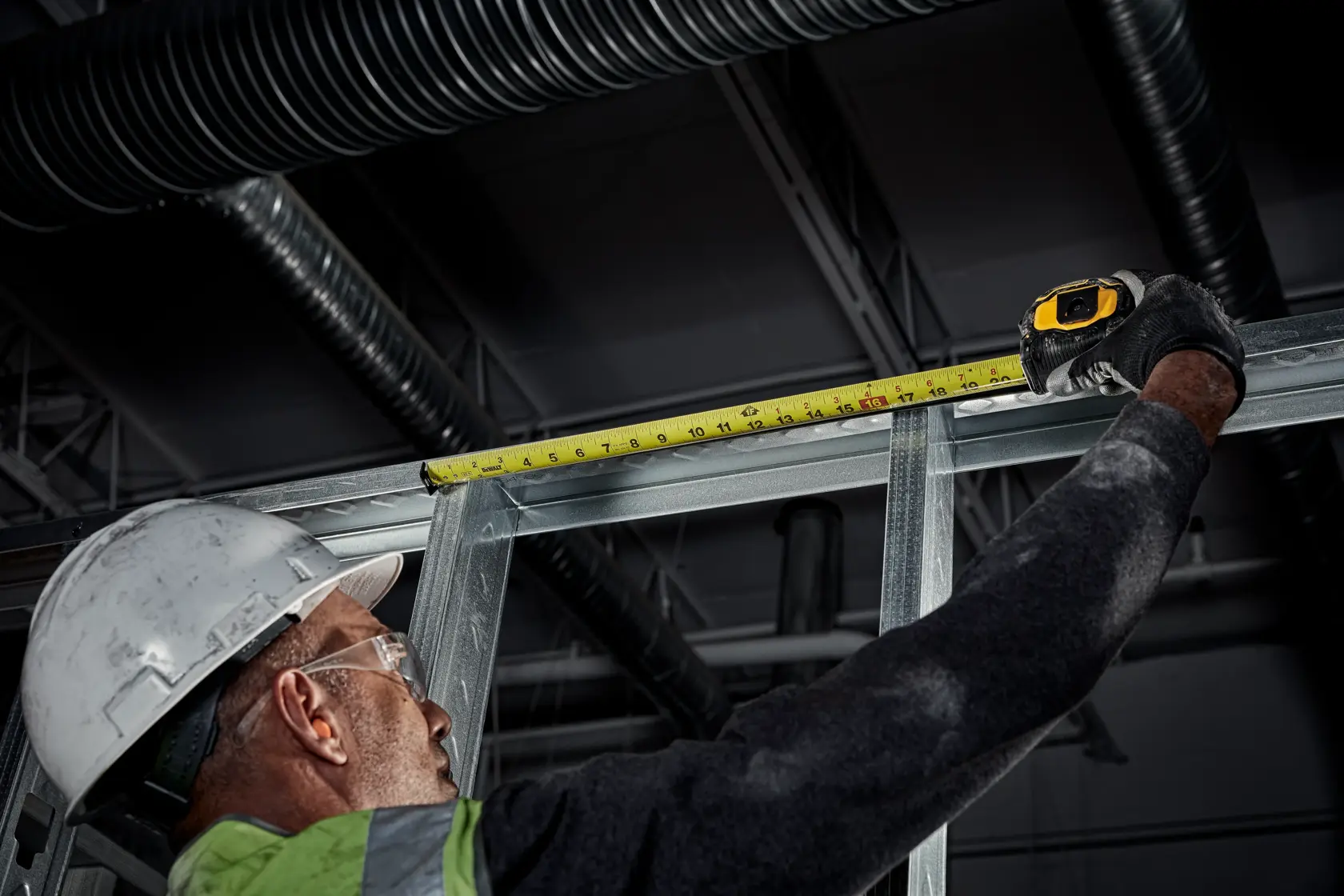 Tough Series 25 feet Tape Measure being used by worker to measure distance between two studs in metal frame at worksite.
