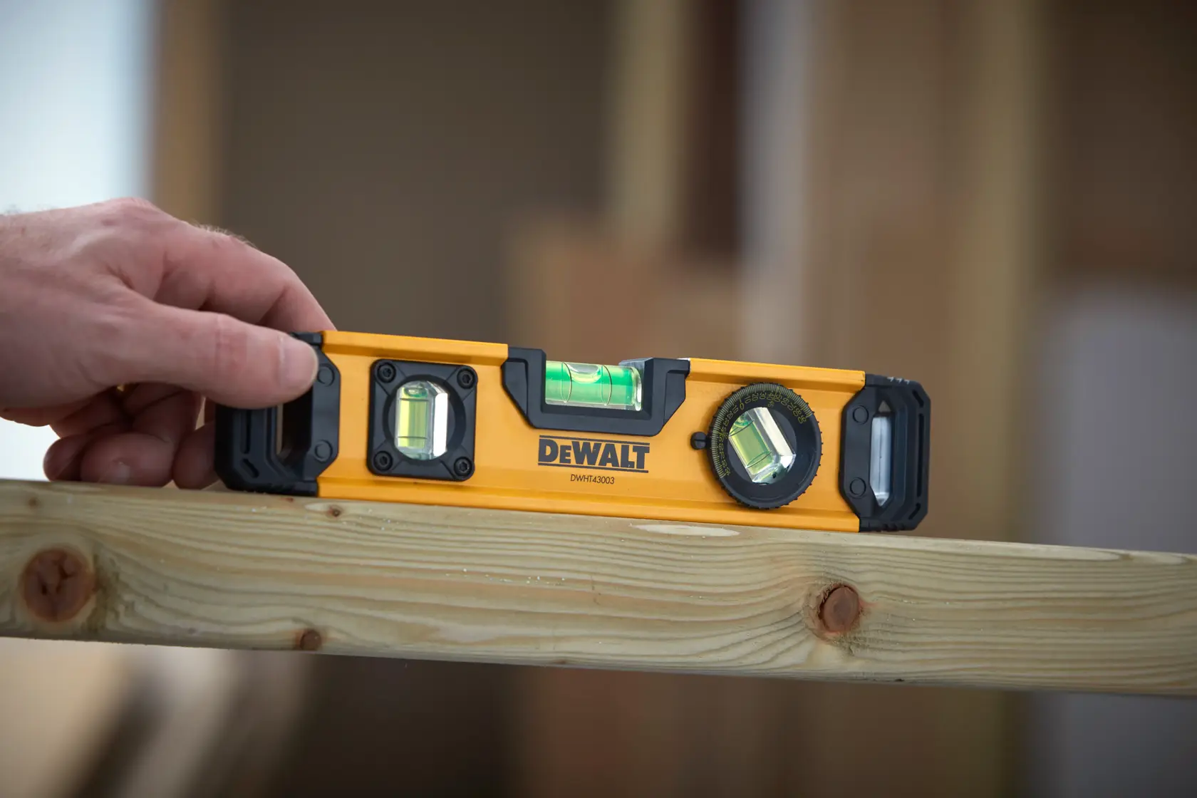 A person holding a DEWALT DWHT43003 spirit level against a wooden beam, with the tool being used to check the levelness of the surface.