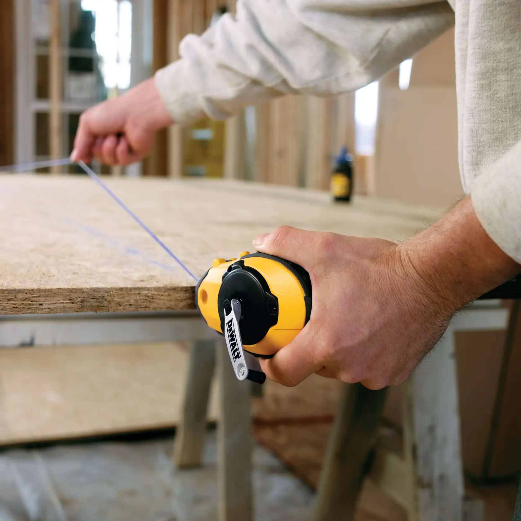 Close up of Reel Kit with Blue Chalk being used by worker to mark line on wooden surface.