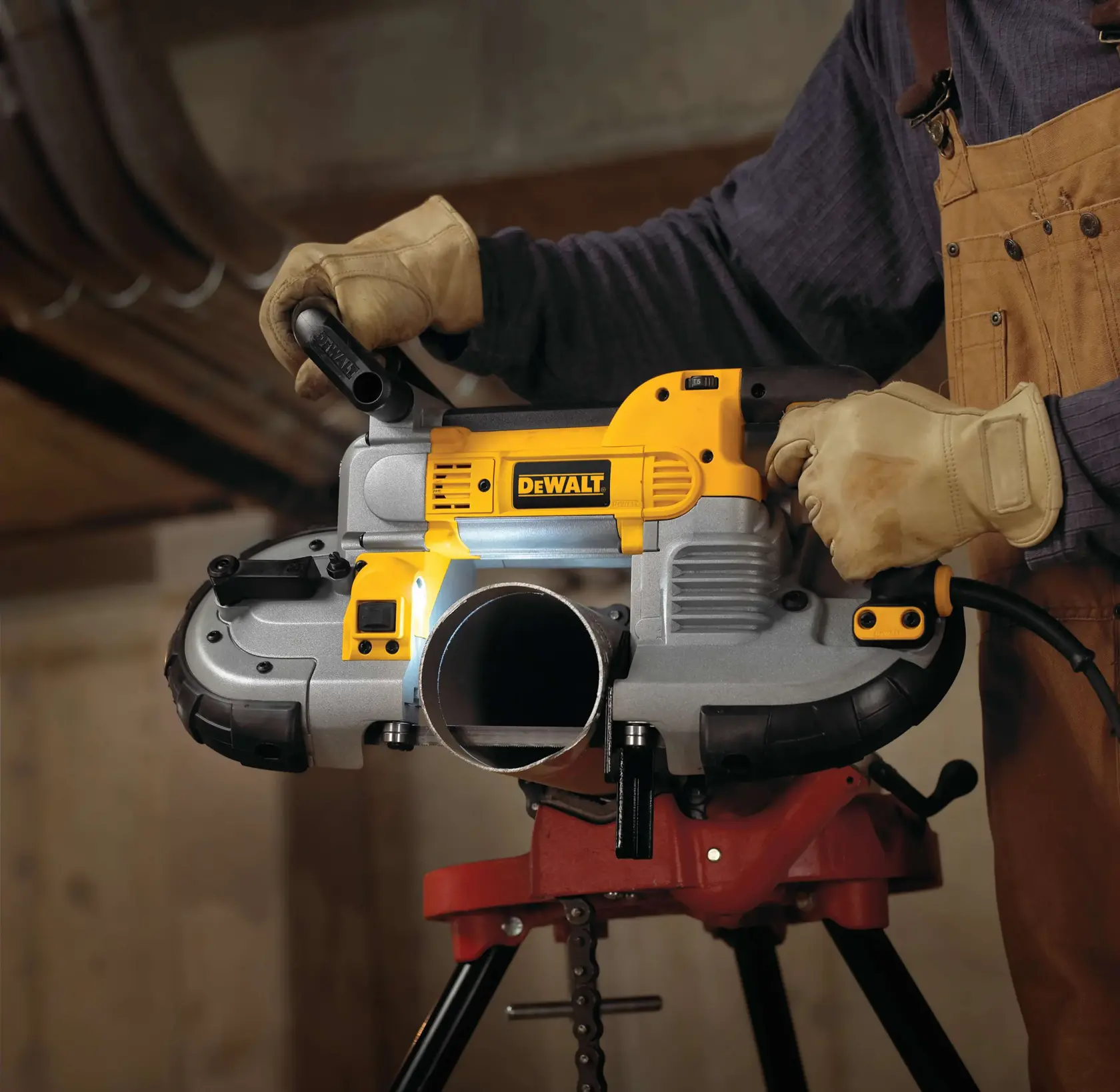 A close-up view of a person using a DEWALT portable band saw to cut a metal pipe in a workshop. The person is wearing gloves and a brown work apron.