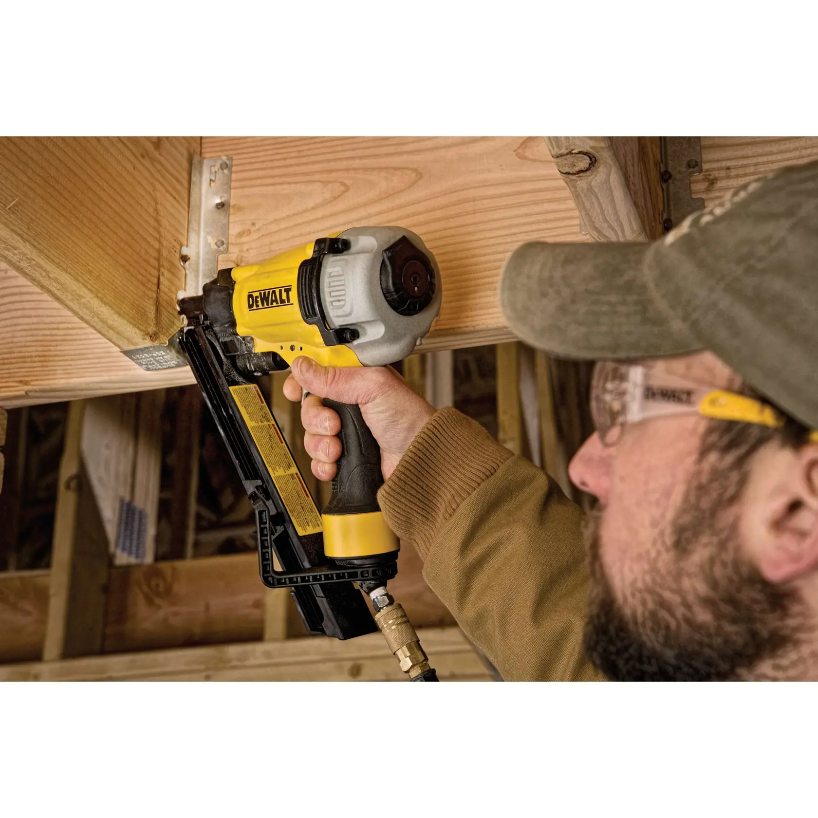A person using a DEWALT pneumatic nail gun to secure wood framing during construction. The tool is yellow and black, and connected to an air hose.
