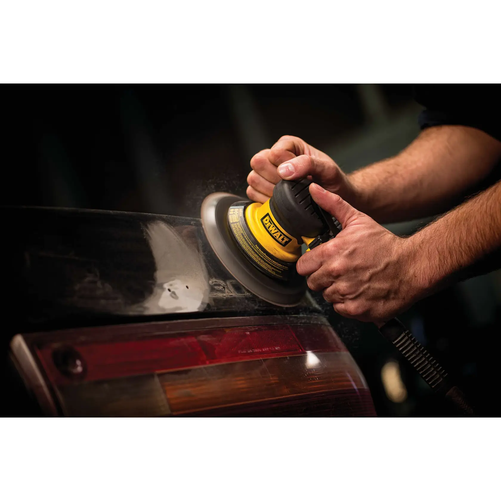 Close-up of hands using a DEWALT pneumatic sander to polish the surface of a car's rear area.