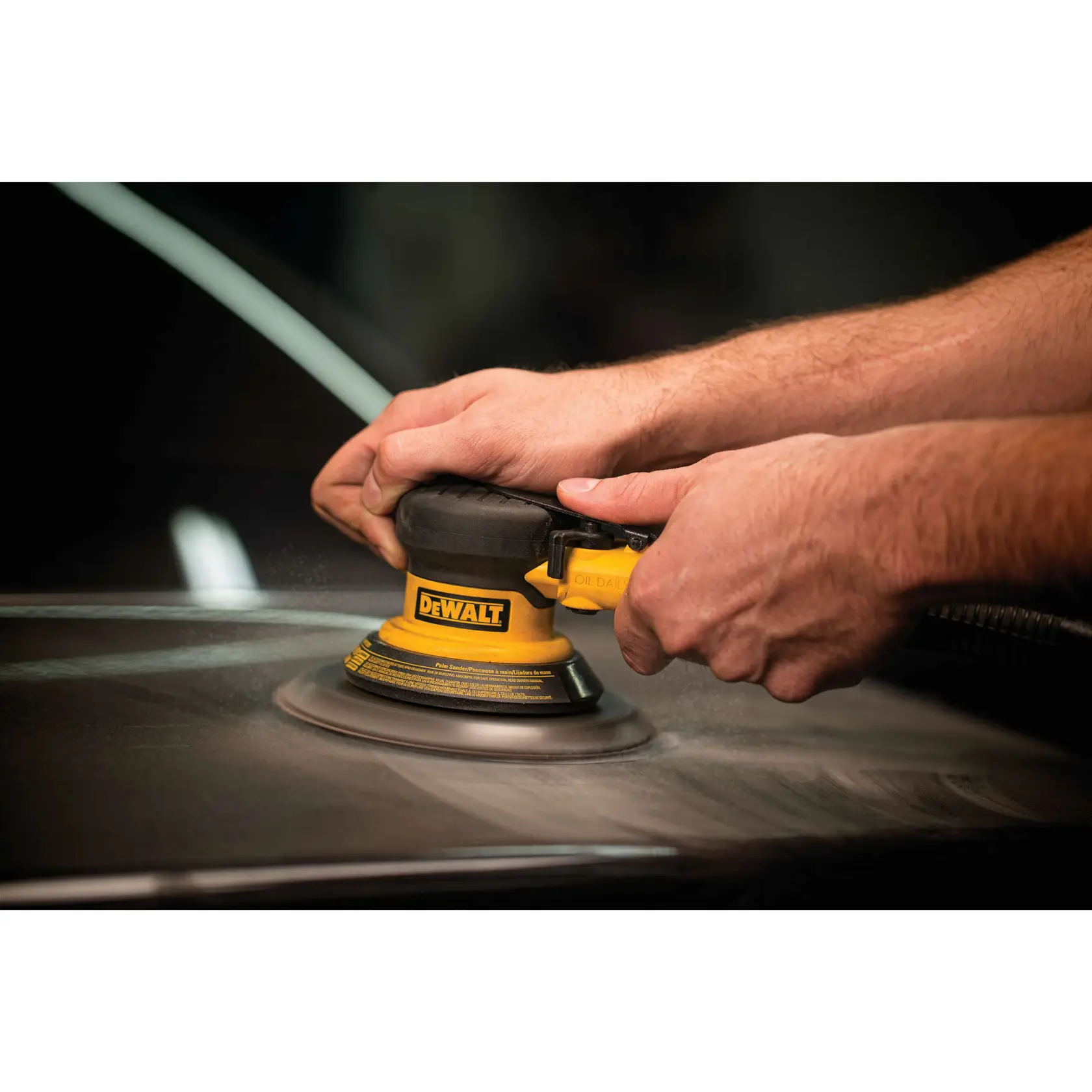 Close-up of hands operating a DEWALT orbital sander on a flat surface.