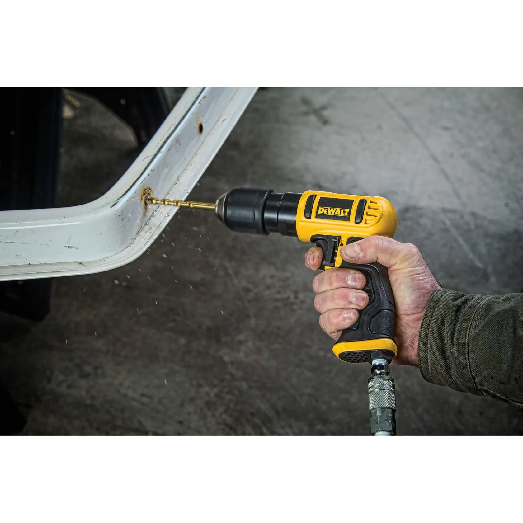A person using a DEWALT pneumatic drill to drill a hole into a white metal surface, with metal shavings visible.