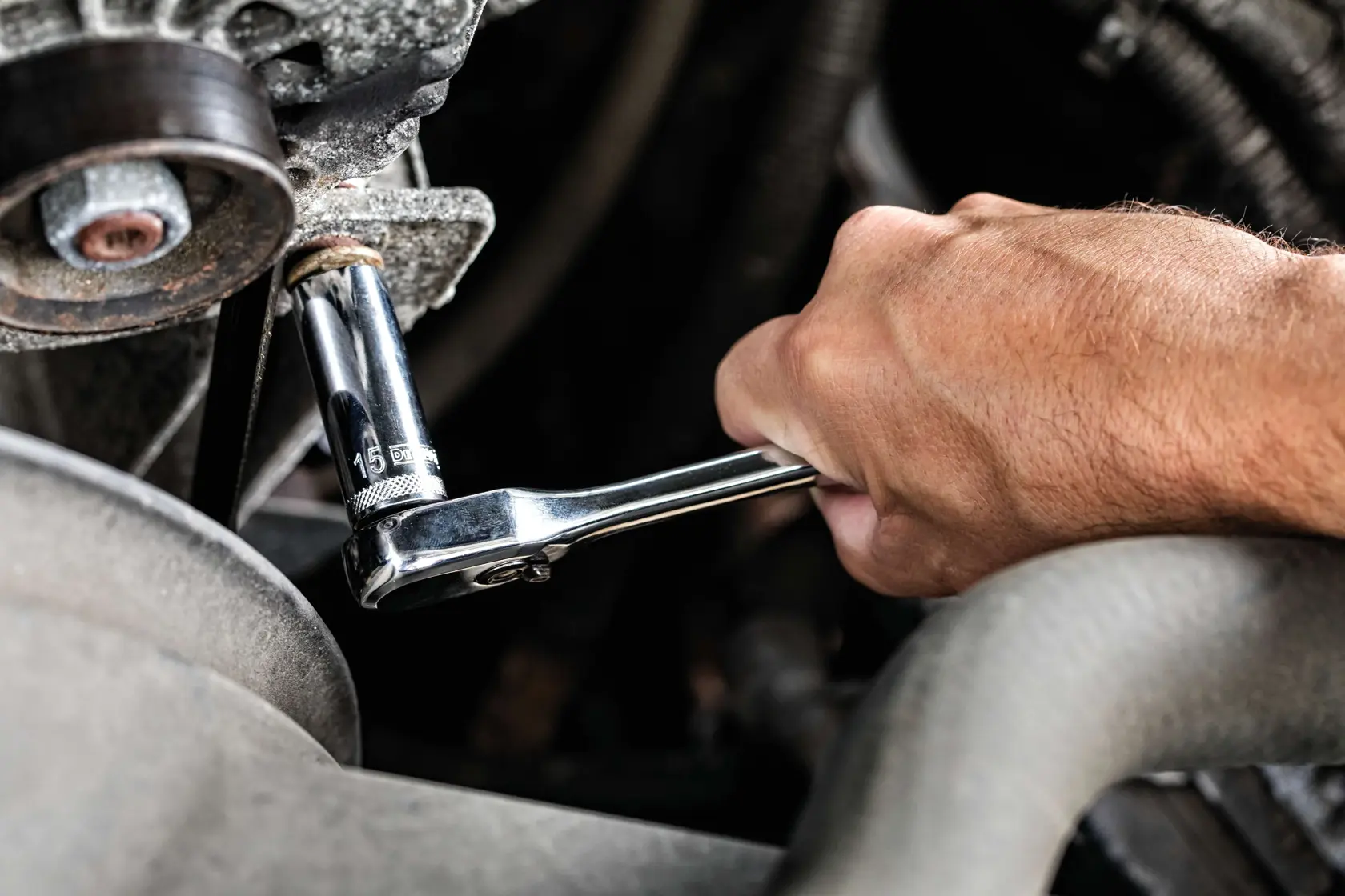 A close-up of a hand using a DEWALT ratchet wrench with a 15mm socket to tighten or loosen a bolt on a piece of machinery or vehicle engine.