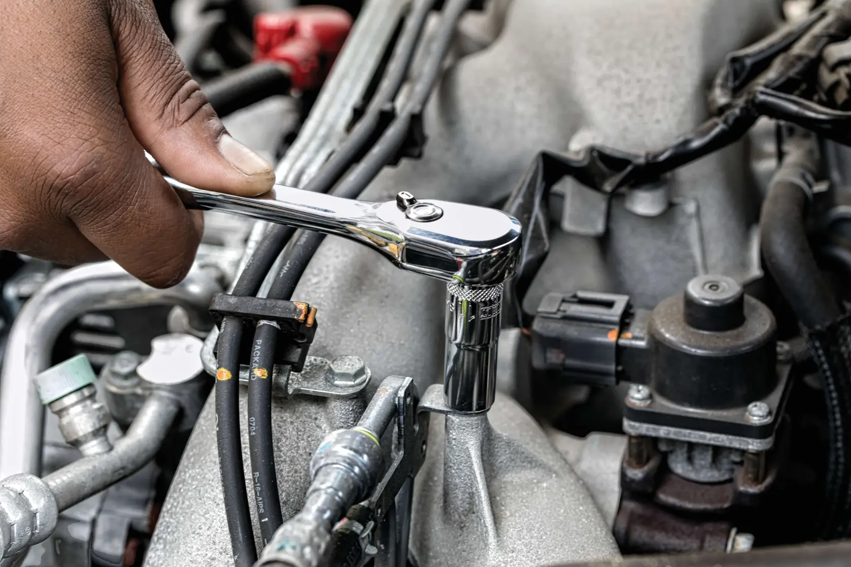 A person using a DEWALT ratchet wrench to tighten or loosen a bolt on a car engine part.