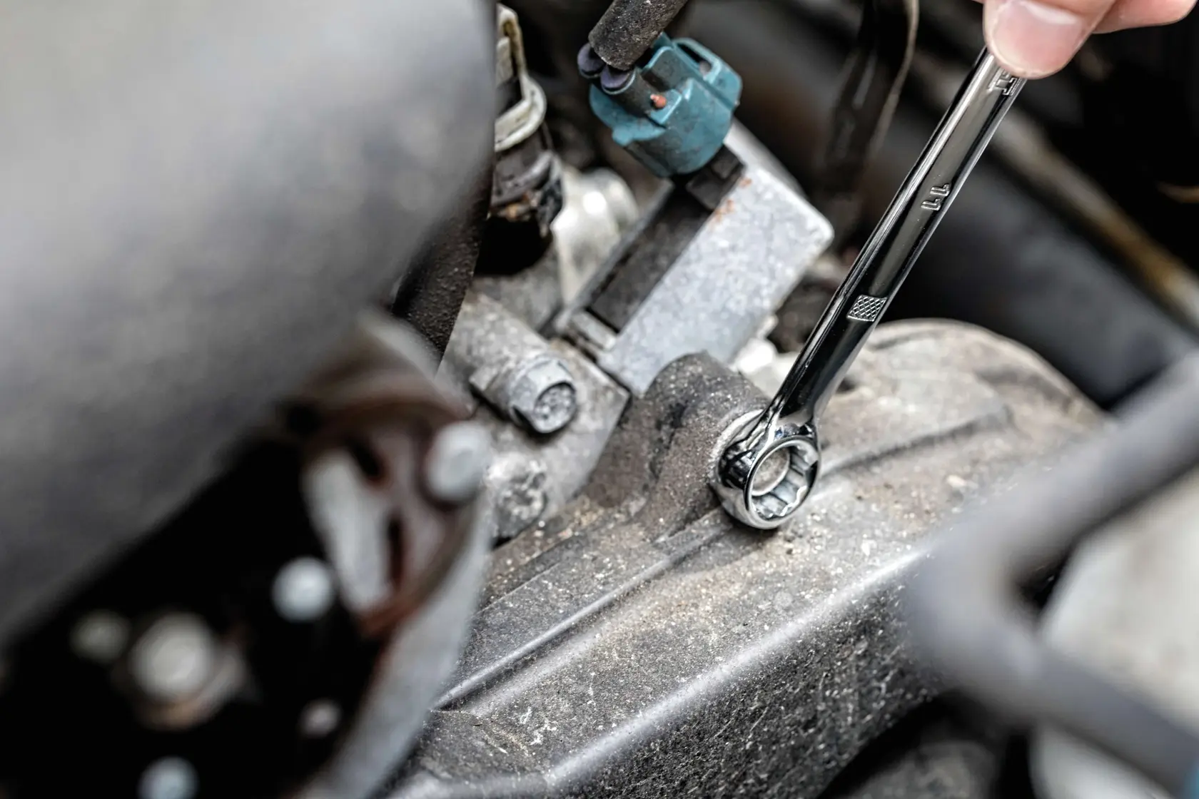 A close-up view of a hand using a DEWALT ratcheting wrench to tighten or loosen a bolt on a dirty engine part.