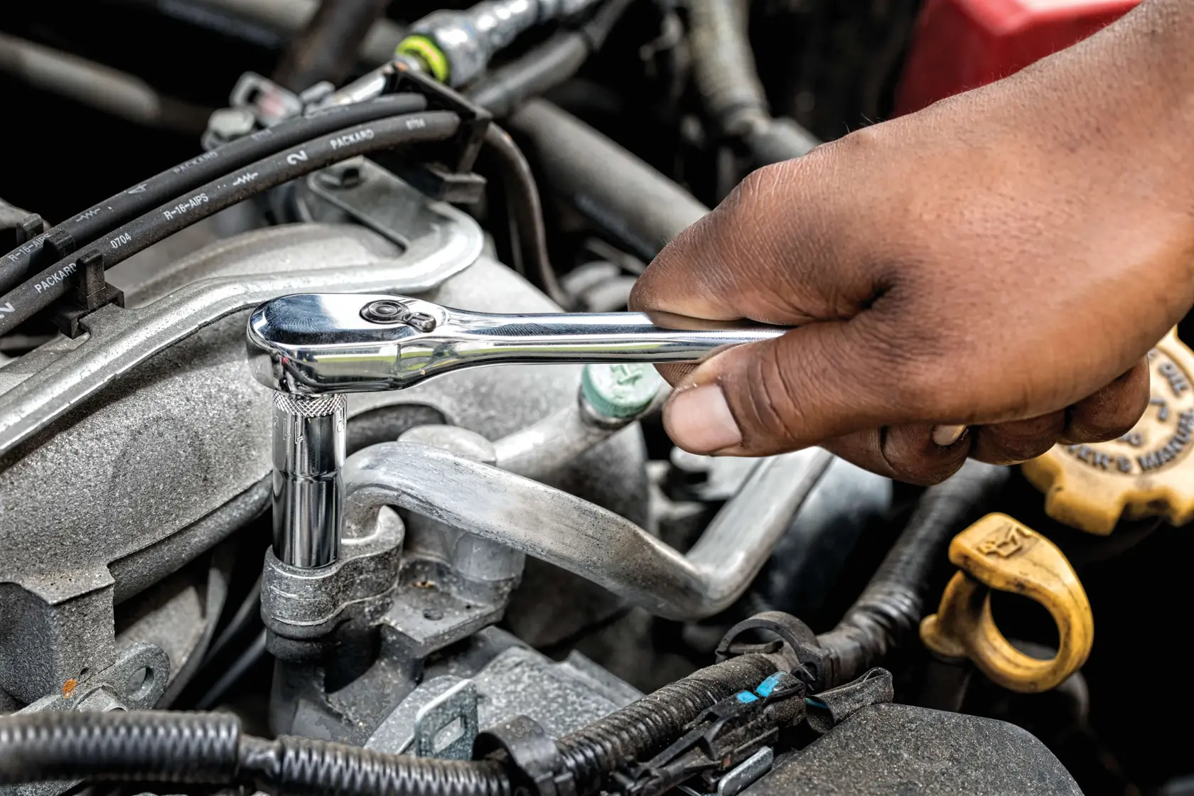 A person uses a DEWALT ratchet wrench to work on an automotive engine, tightening or loosening a bolt.