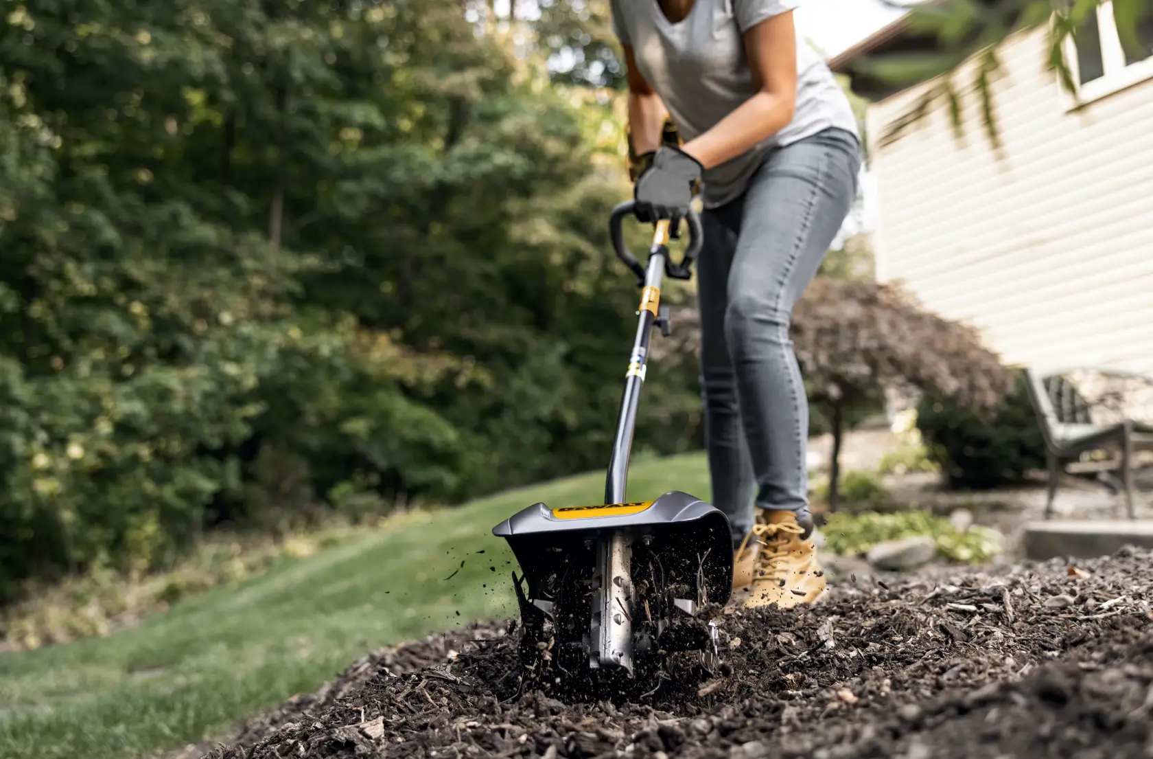 DEWALT cultivator attachment headf ront view tending to mulch in backyard in gray shirt and jeans