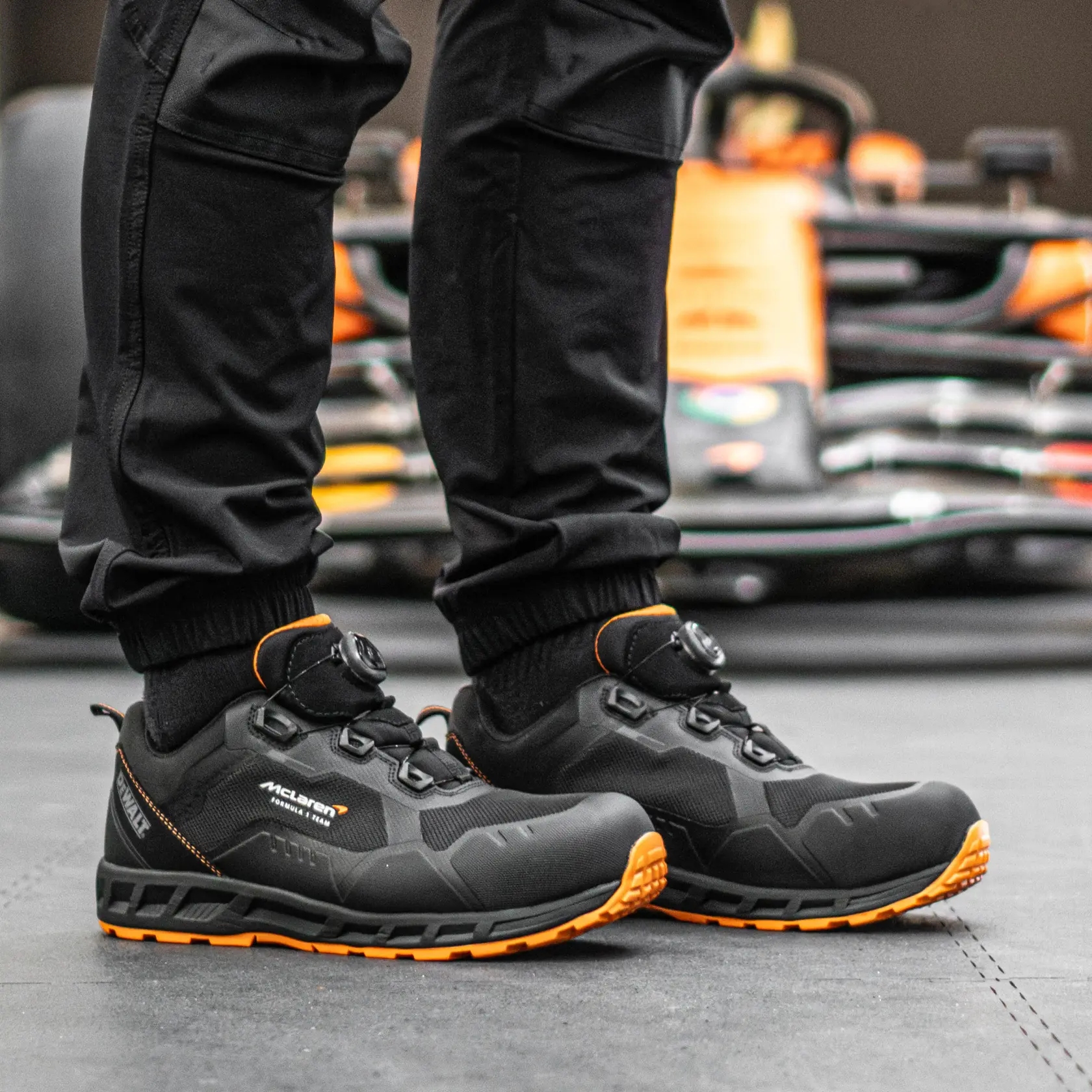 Side view facing right of the DEWALT x McLaren Torque Men's Safety Shoes in black on model on location