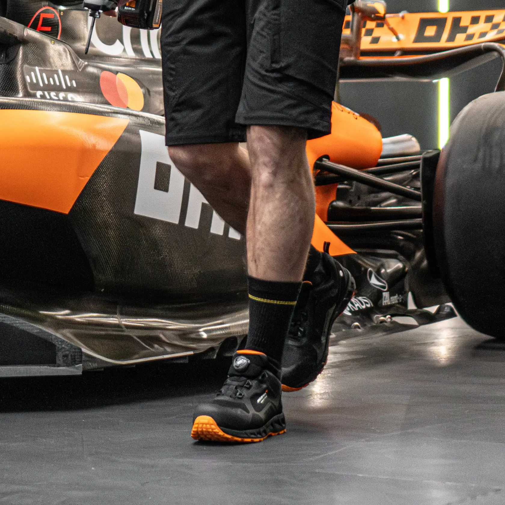 Side view facing left of the DEWALT x McLaren Torque Men's Safety Shoes in black on model on location