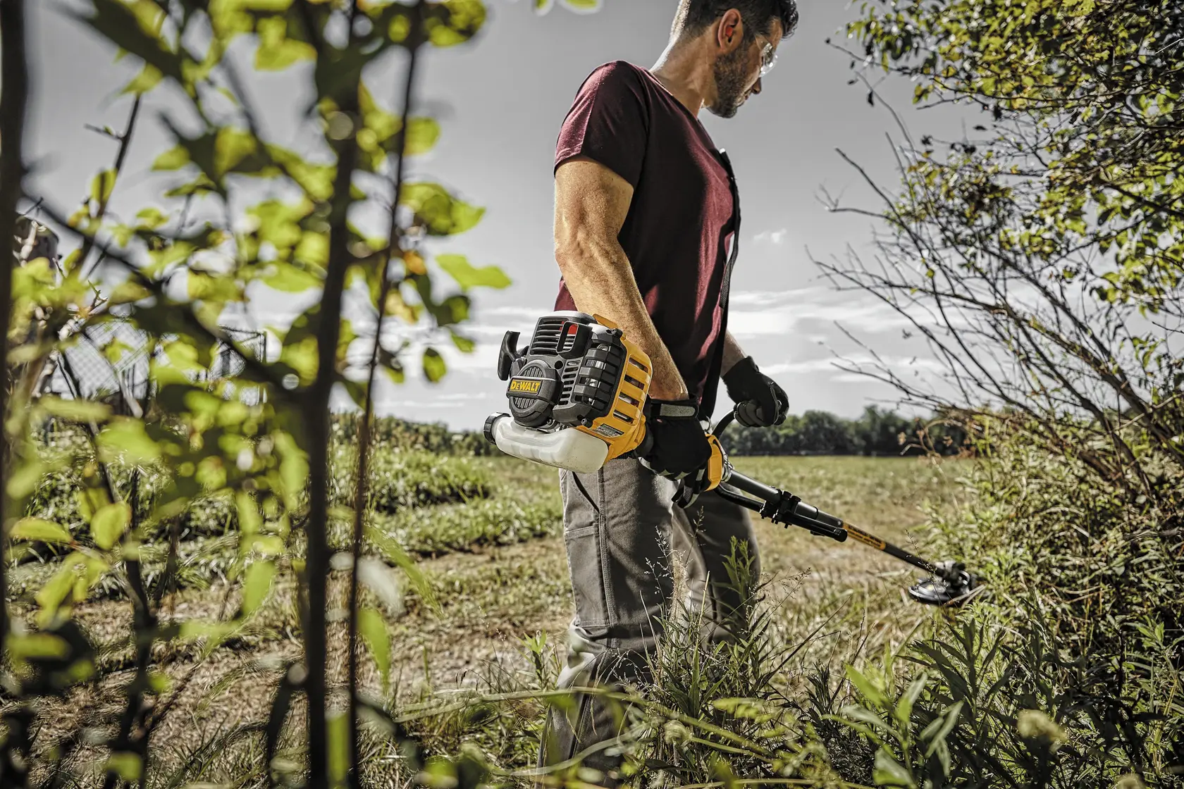 Gas Brushcutter with Attachment Capability being used by person to cut overgrowth outdoors.
