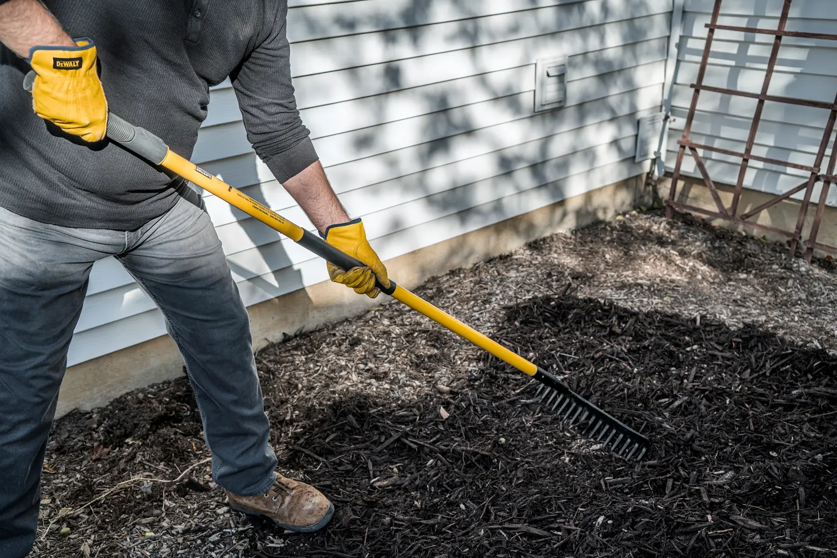 60 inch Fiberglass Handle 16-Tine Bow Rake in side view raking mulch in gray shirt and pants